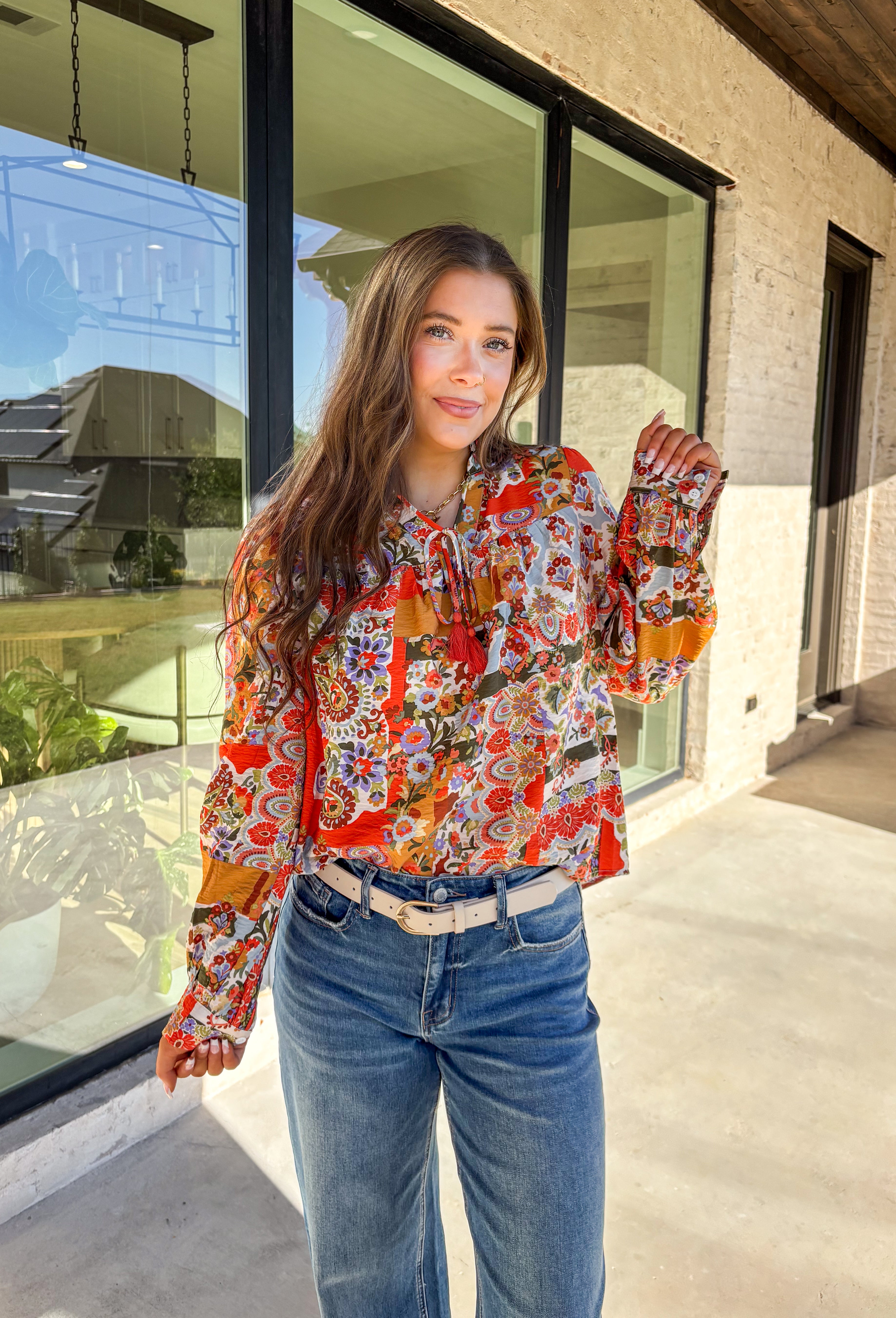 Bring bold color and cheerful energy to your fall wardrobe with this long sleeve floral top by Fate. The mix of orange, off white, tan, brown, purple, and blue creates a stunning statement print that feels both playful and timeless. Designed with a subtle ruffle neckline and a front tie detail, this blouse adds a soft feminine finish to your everyday look.