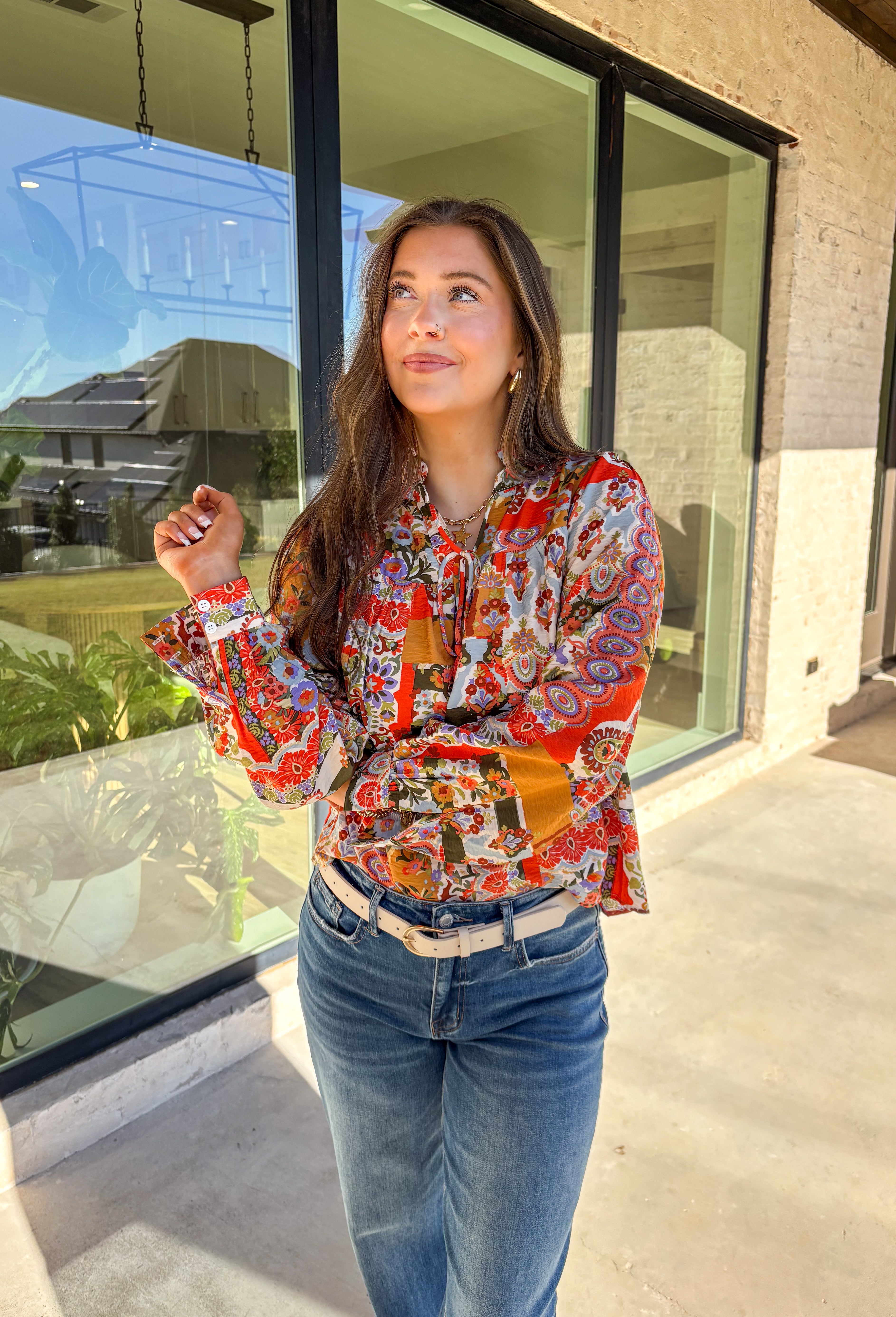 Bring bold color and cheerful energy to your fall wardrobe with this long sleeve floral top by Fate. The mix of orange, off white, tan, brown, purple, and blue creates a stunning statement print that feels both playful and timeless. Designed with a subtle ruffle neckline and a front tie detail, this blouse adds a soft feminine finish to your everyday look.