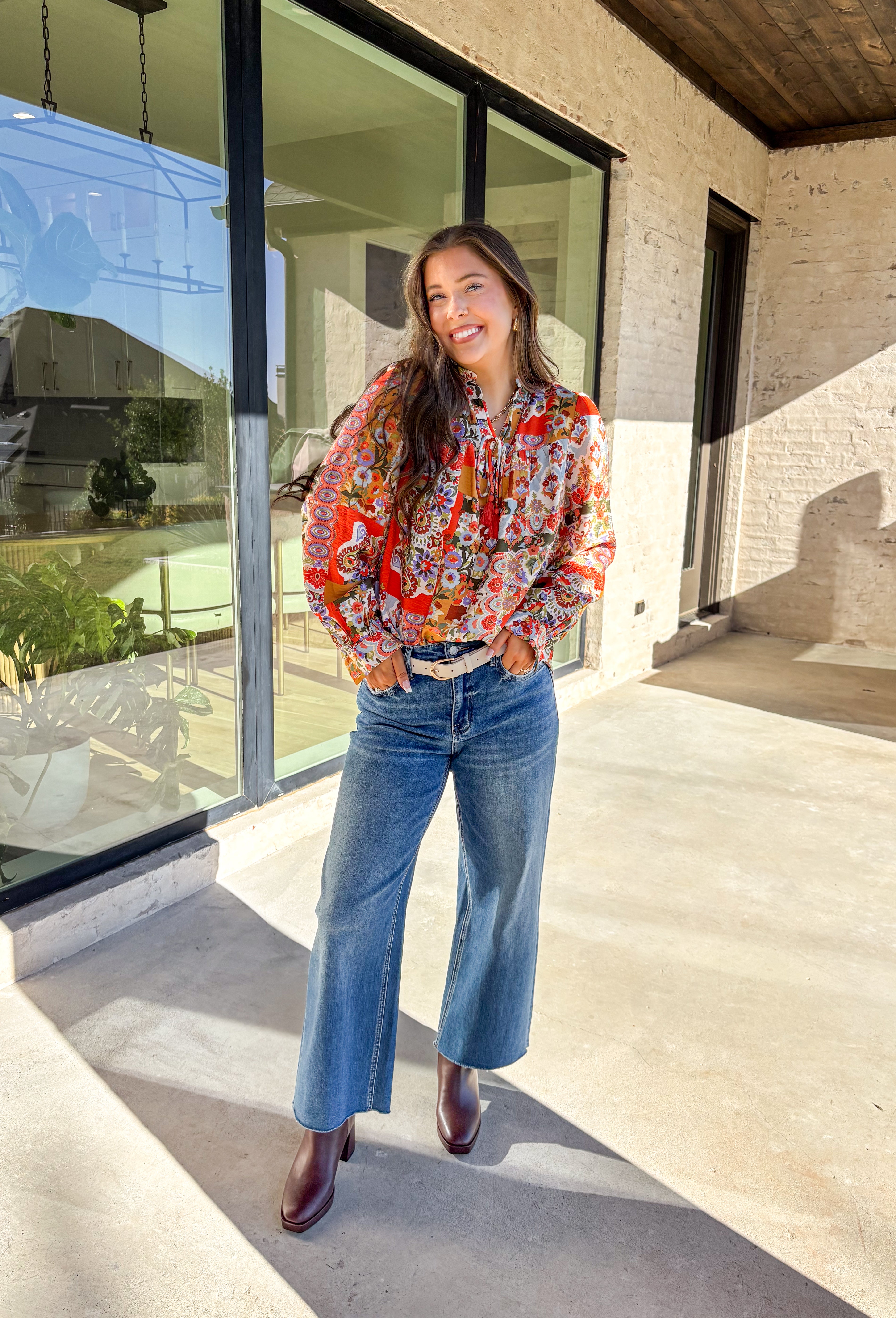 Bring bold color and cheerful energy to your fall wardrobe with this long sleeve floral top by Fate. The mix of orange, off white, tan, brown, purple, and blue creates a stunning statement print that feels both playful and timeless. Designed with a subtle ruffle neckline and a front tie detail, this blouse adds a soft feminine finish to your everyday look.