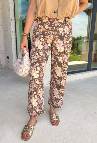 Give your fall wardrobe a fresh update with these beautifully printed floral pants. Featuring a rich brown backdrop with a bold neutral floral print, these statement pants are the perfect blend of timeless and trendy. Front seam detailing creates a flattering, elongated silhouette, while the classic zip-fly, button closure, and belt loops make them easy to style with all your favorite seasonal tops and sweaters. 