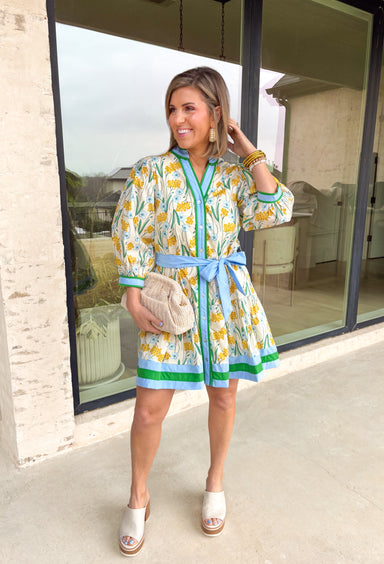 Fresh, bright, and effortlessly polished, this neutral long sleeve button-down dress is made for spring days when you want to feel put together without trying too hard. Featuring a yellow and blue floral print with pops of green, it brings the prettiest burst of color to a soft neutral base. Blue and green band detailing along the neckline and down the front adds a bold, flattering accent, with matching trim at the cuffs and hem for a pulled-together finish. 