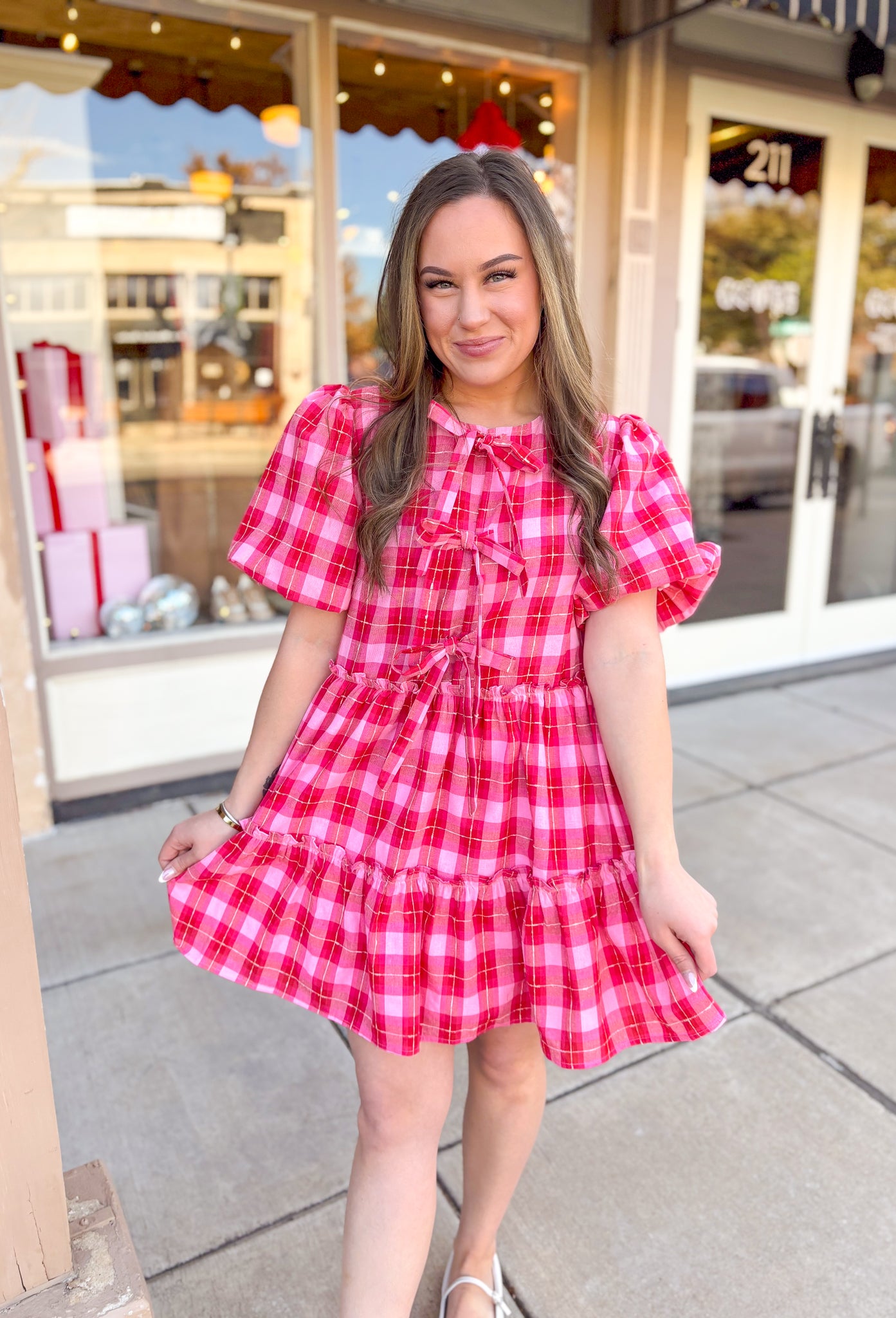 Red and pink plaid mini dress with short puff sleeves and bow detail on the front with a tiered skirt.