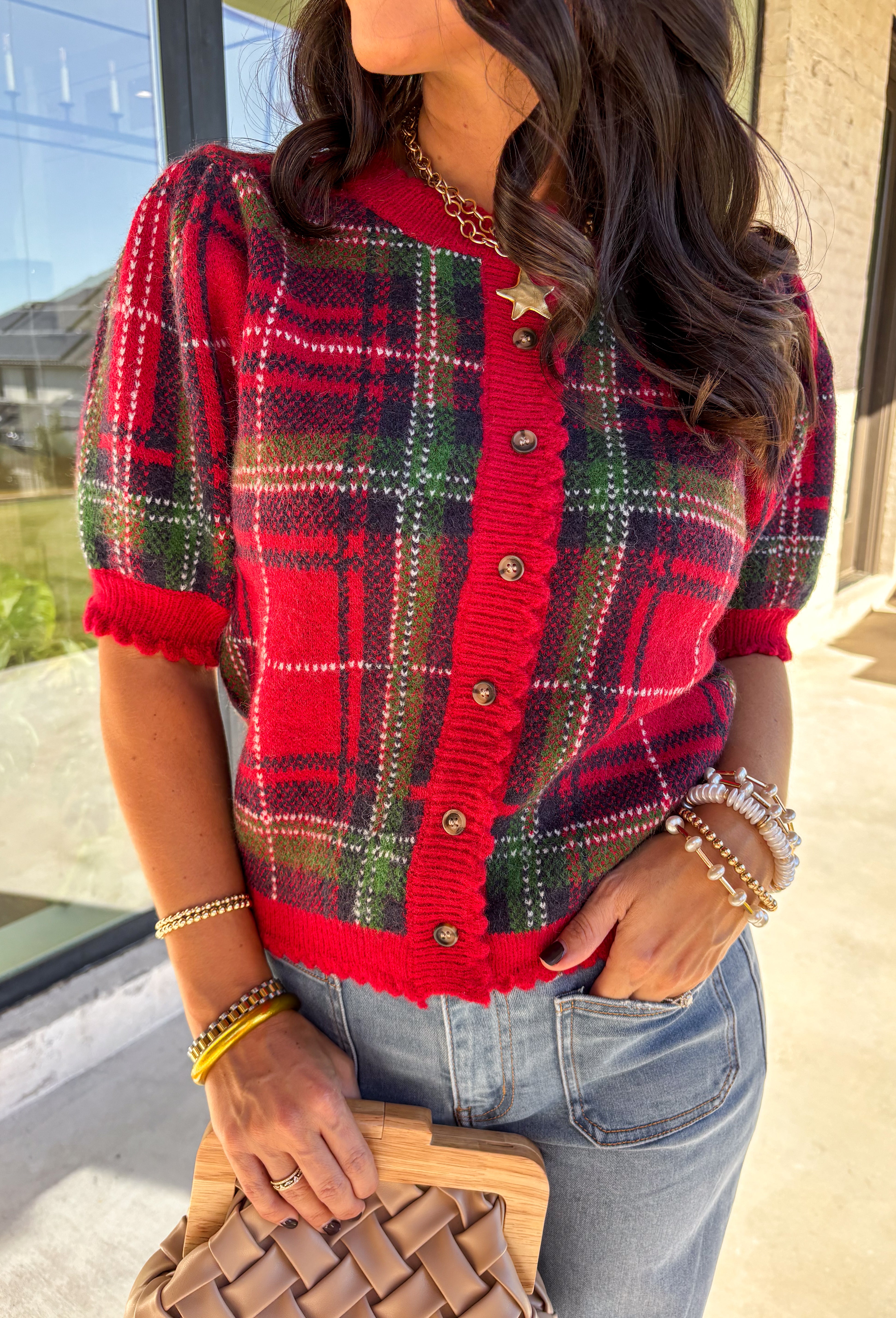 Festive and cozy, this plaid sweater knit top is made to bring holiday cheer. Featuring short puff sleeves and a scallop edge neckline, it’s finished with a button-front closure for a cardigan-style fit. The bold red plaid pattern in holiday tones makes it a standout for seasonal gatherings, while the soft knit keeps it comfortable and easy to wear. Perfect for layering or styling on its own, this cardigan blends playful charm with cozy comfort.