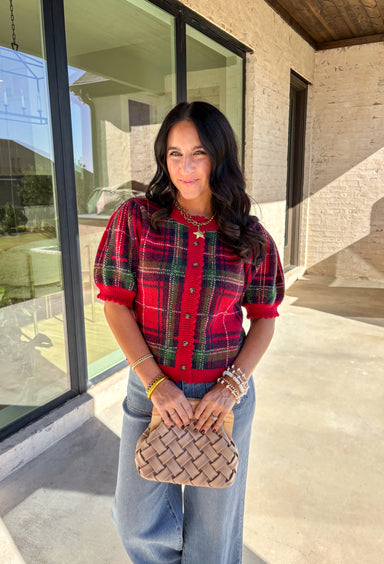 Festive and cozy, this plaid sweater knit top is made to bring holiday cheer. Featuring short puff sleeves and a scallop edge neckline, it’s finished with a button-front closure for a cardigan-style fit. The bold red plaid pattern in holiday tones makes it a standout for seasonal gatherings, while the soft knit keeps it comfortable and easy to wear. Perfect for layering or styling on its own, this cardigan blends playful charm with cozy comfort.