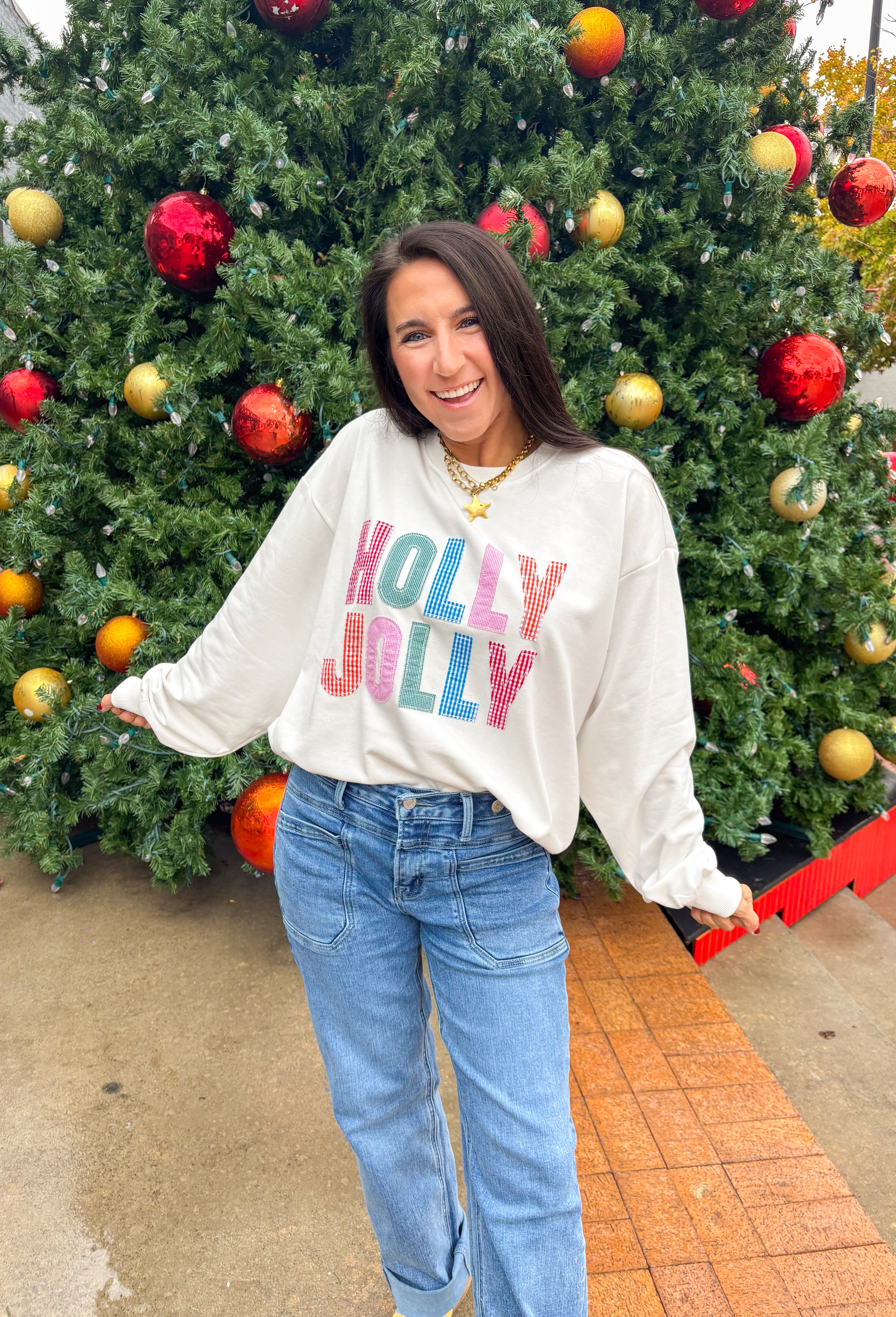 Stay merry and bright this season in the “Holly Jolly” pullover by Main Strip! This soft white lightweight sweatshirt features colorful gingham lettering—each letter a unique mix of festive color and pattern—outlined with white stitching for a playful holiday touch. Cozy and cheerful, it’s the perfect piece for decking the halls, sipping cocoa, or simply spreading a little Christmas joy.