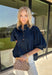 A classic denim top is a wardrobe staple, and this beautifully detailed top from Entro is one you'll wear on repeat. Designed in a rich dark wash denim, this timeless piece features a gold button-front design that makes it easy to style for any occasion. The ¾ puff sleeves add a feminine touch, while the self-tie cuffs create a charming finishing detail.