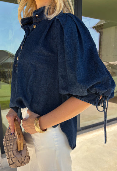 A classic denim top is a wardrobe staple, and this beautifully detailed top from Entro is one you'll wear on repeat. Designed in a rich dark wash denim, this timeless piece features a gold button-front design that makes it easy to style for any occasion. The ¾ puff sleeves add a feminine touch, while the self-tie cuffs create a charming finishing detail.