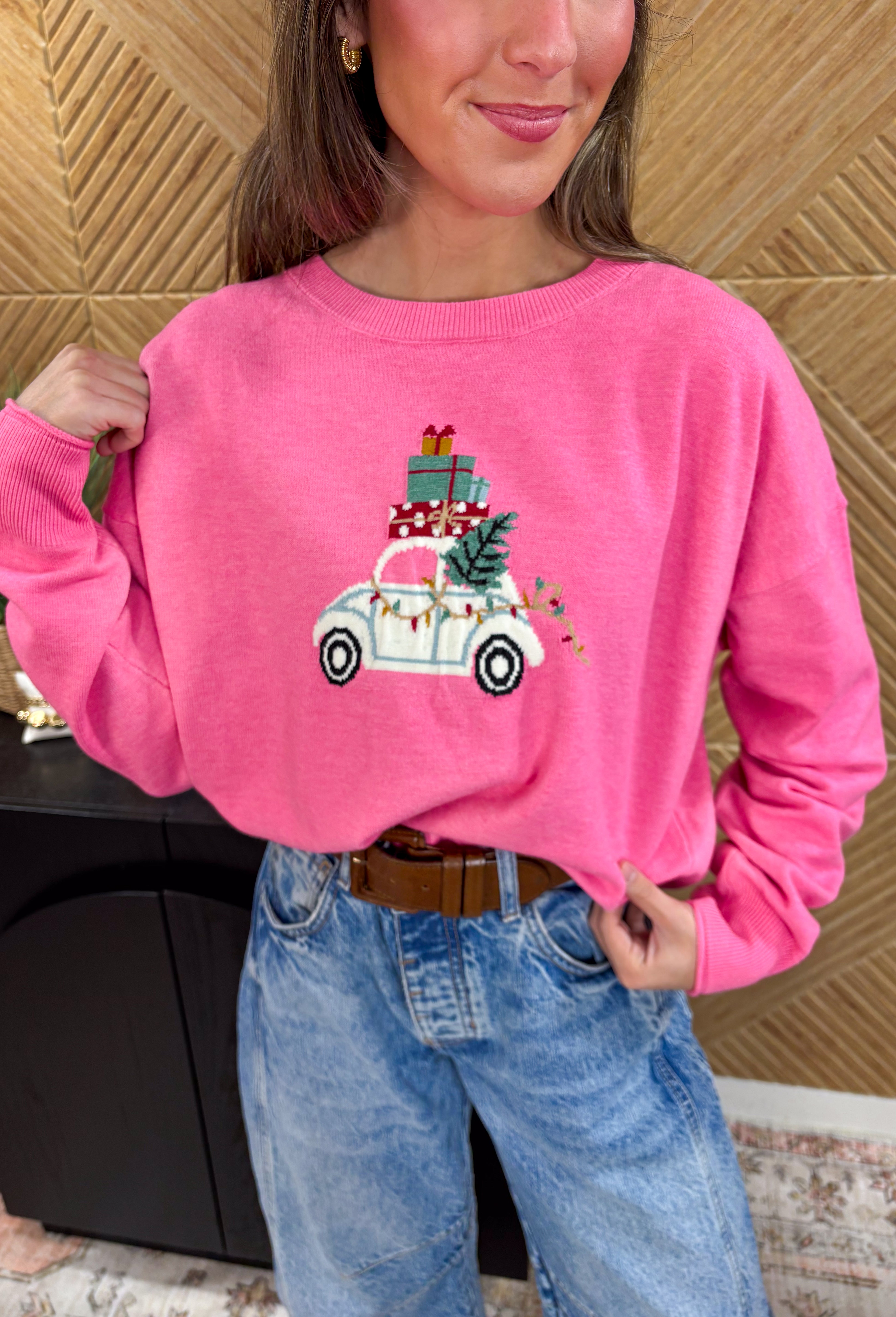 Bring the festive fun with this adorable pink holiday sweater by Sunday Edition! Featuring a white slug bug design complete with a Christmas tree hanging out the back, presents stacked on top, and colorful string lights along the side, this playful knit captures all the magic of the season. Soft, cozy, and full of charm, it’s the perfect sweater for cookie decorating, holiday parties, or any moment that needs a little extra cheer.