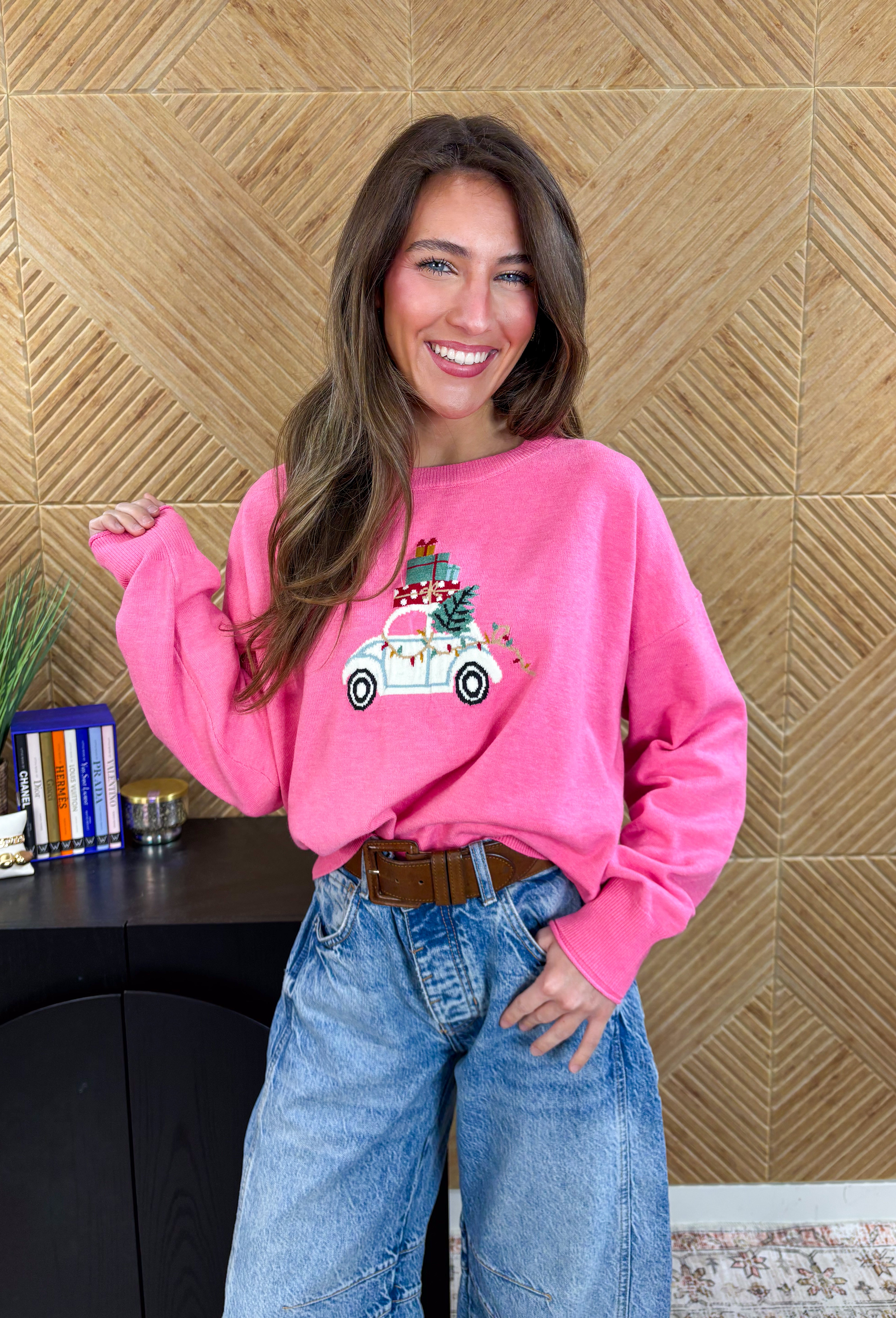 Bring the festive fun with this adorable pink holiday sweater by Sunday Edition! Featuring a white slug bug design complete with a Christmas tree hanging out the back, presents stacked on top, and colorful string lights along the side, this playful knit captures all the magic of the season. Soft, cozy, and full of charm, it’s the perfect sweater for cookie decorating, holiday parties, or any moment that needs a little extra cheer.