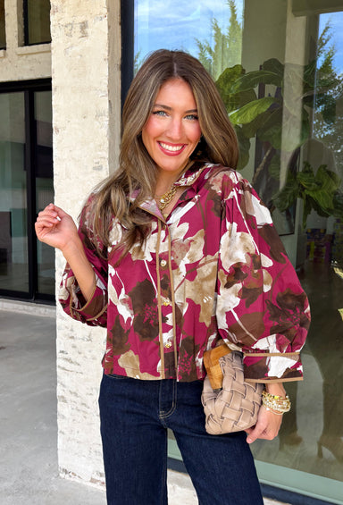 Deep merlot brings a rich seasonal feel to this floral top from Entro. The neutral floral print softens the bold background with warm, easy-to-style shades that fit beautifully into a late-fall wardrobe. A high neckline and button-front closure give the top a classic look, while contrast trim adds another eye-catching detail. The ¾ puff sleeves are finished with buttoned cuffs, and gathering along the back yoke adds subtle shape and movement. 