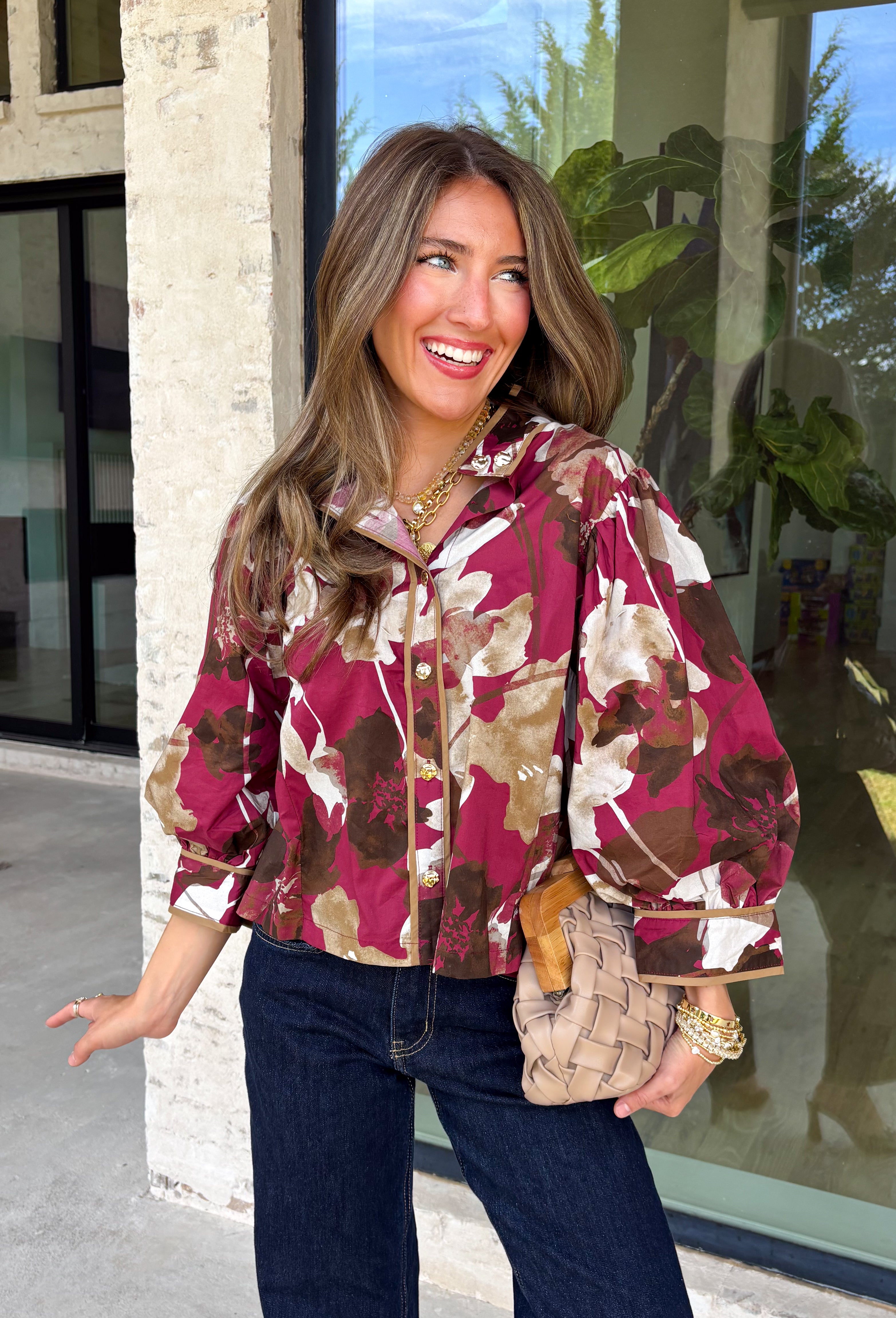 Deep merlot brings a rich seasonal feel to this floral top from Entro. The neutral floral print softens the bold background with warm, easy-to-style shades that fit beautifully into a late-fall wardrobe. A high neckline and button-front closure give the top a classic look, while contrast trim adds another eye-catching detail. The ¾ puff sleeves are finished with buttoned cuffs, and gathering along the back yoke adds subtle shape and movement. 