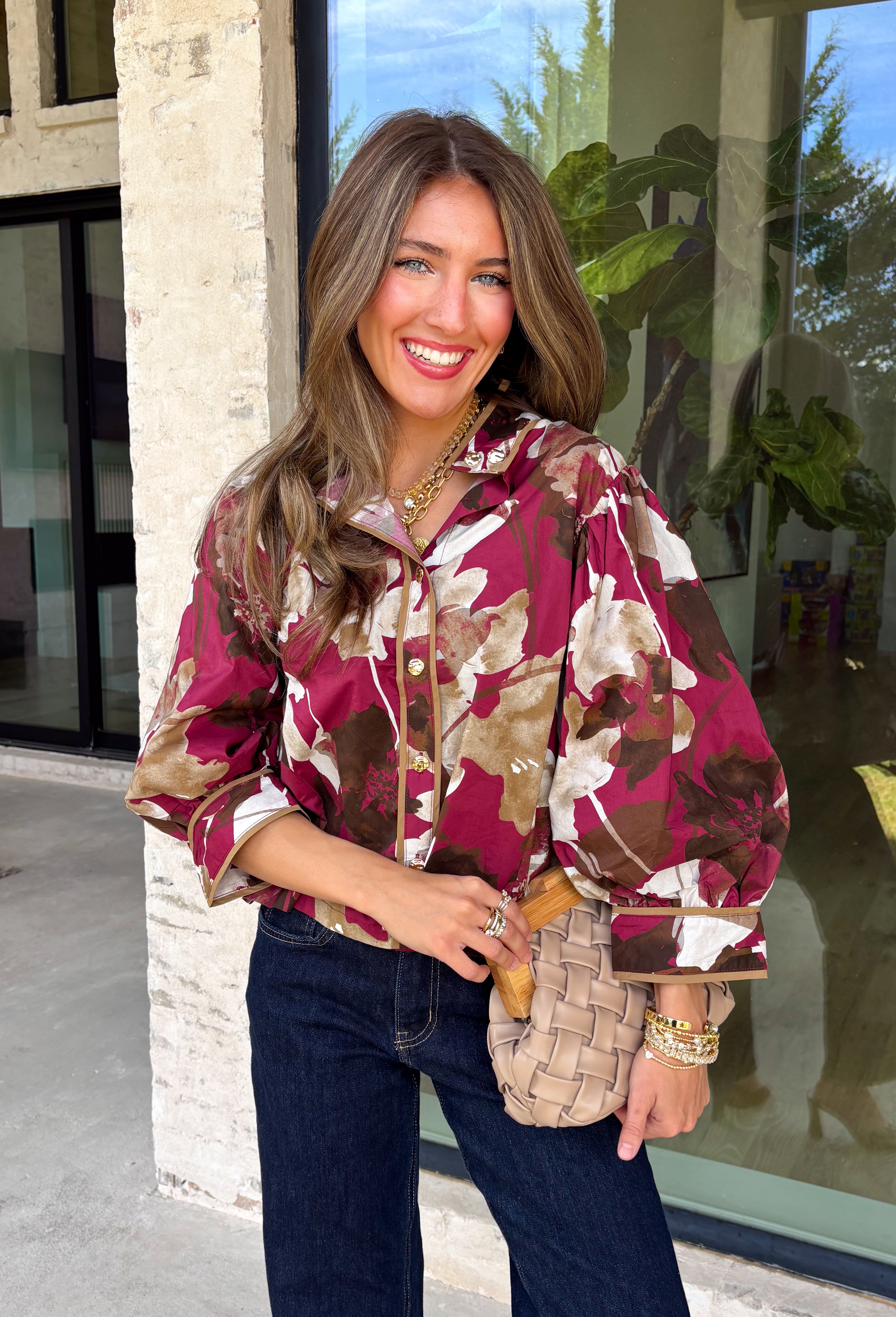 Deep merlot brings a rich seasonal feel to this floral top from Entro. The neutral floral print softens the bold background with warm, easy-to-style shades that fit beautifully into a late-fall wardrobe. A high neckline and button-front closure give the top a classic look, while contrast trim adds another eye-catching detail. The ¾ puff sleeves are finished with buttoned cuffs, and gathering along the back yoke adds subtle shape and movement. 