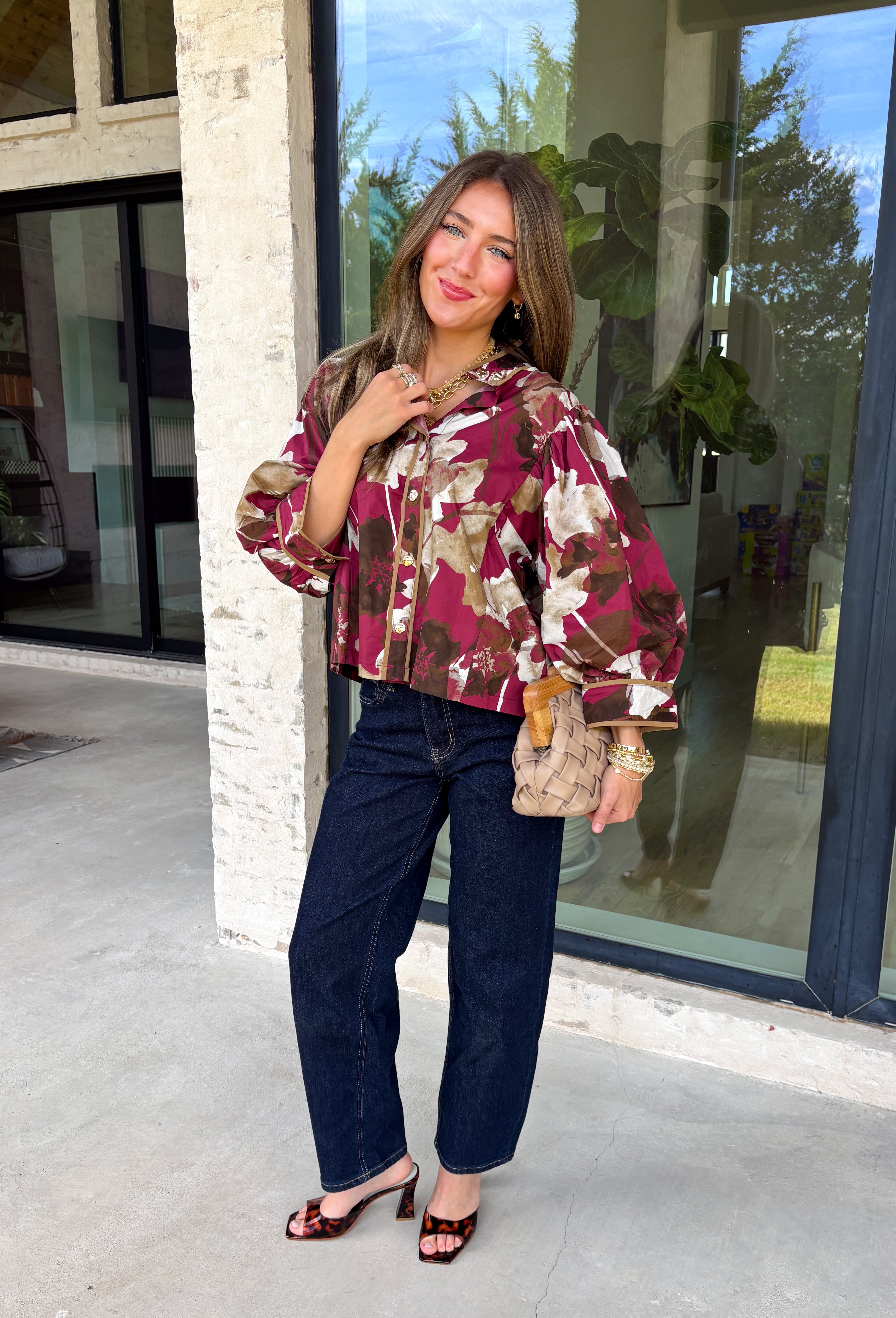 Deep merlot brings a rich seasonal feel to this floral top from Entro. The neutral floral print softens the bold background with warm, easy-to-style shades that fit beautifully into a late-fall wardrobe. A high neckline and button-front closure give the top a classic look, while contrast trim adds another eye-catching detail. The ¾ puff sleeves are finished with buttoned cuffs, and gathering along the back yoke adds subtle shape and movement. 