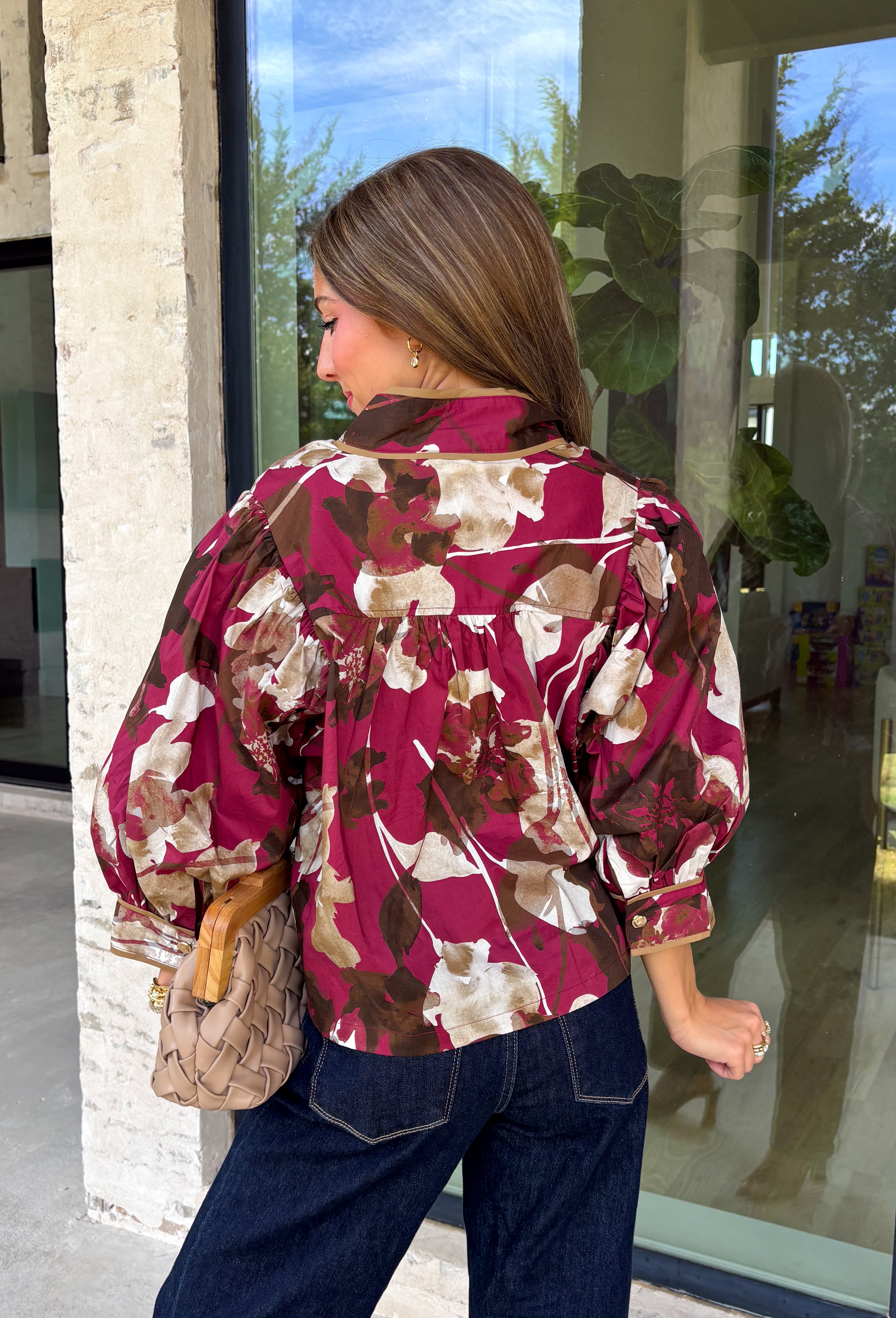 Deep merlot brings a rich seasonal feel to this floral top from Entro. The neutral floral print softens the bold background with warm, easy-to-style shades that fit beautifully into a late-fall wardrobe. A high neckline and button-front closure give the top a classic look, while contrast trim adds another eye-catching detail. The ¾ puff sleeves are finished with buttoned cuffs, and gathering along the back yoke adds subtle shape and movement. 
