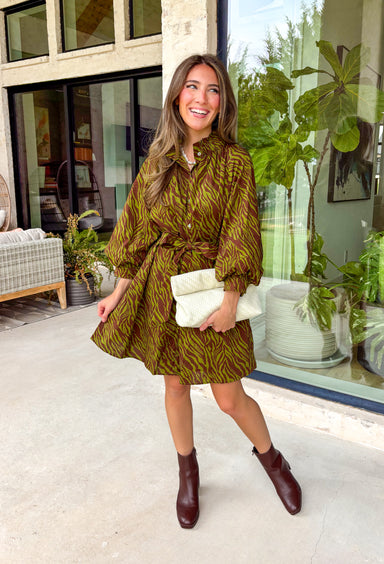 A timeless print meets effortless sophistication in this stunning long sleeve dress. Designed in a rich olive hue with a brown zebra print, this dress offers a fresh take on a classic fall look. The button-front design and matching self-tie belt create a flattering, customizable silhouette, while the soft ruffle neckline adds just the right touch of feminine charm. 