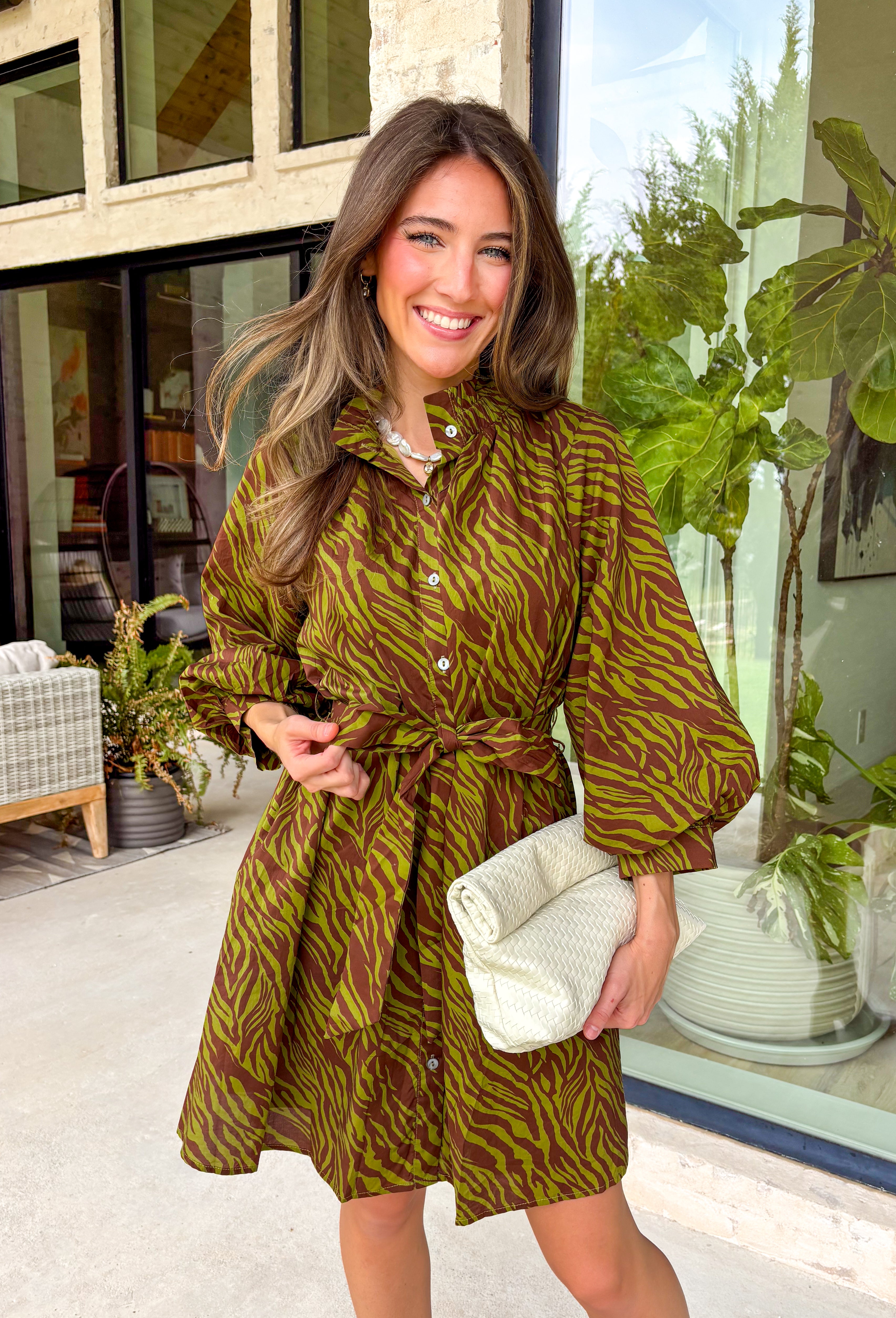 A timeless print meets effortless sophistication in this stunning long sleeve dress. Designed in a rich olive hue with a brown zebra print, this dress offers a fresh take on a classic fall look. The button-front design and matching self-tie belt create a flattering, customizable silhouette, while the soft ruffle neckline adds just the right touch of feminine charm. 