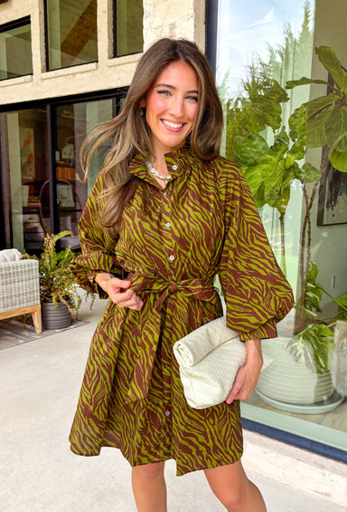 A timeless print meets effortless sophistication in this stunning long sleeve dress. Designed in a rich olive hue with a brown zebra print, this dress offers a fresh take on a classic fall look. The button-front design and matching self-tie belt create a flattering, customizable silhouette, while the soft ruffle neckline adds just the right touch of feminine charm. 