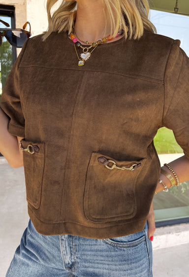 Elevate your autumn wardrobe with a top that's equal parts sophisticated and effortlessly wearable! Crafted from buttery-soft chocolate brown faux suede, this elevated piece brings rich texture and timeless style to any outfit. The standout gold horse bit details on the front pockets add an elegant equestrian-inspired touch, while the sleek back zipper closure creates a polished finish.