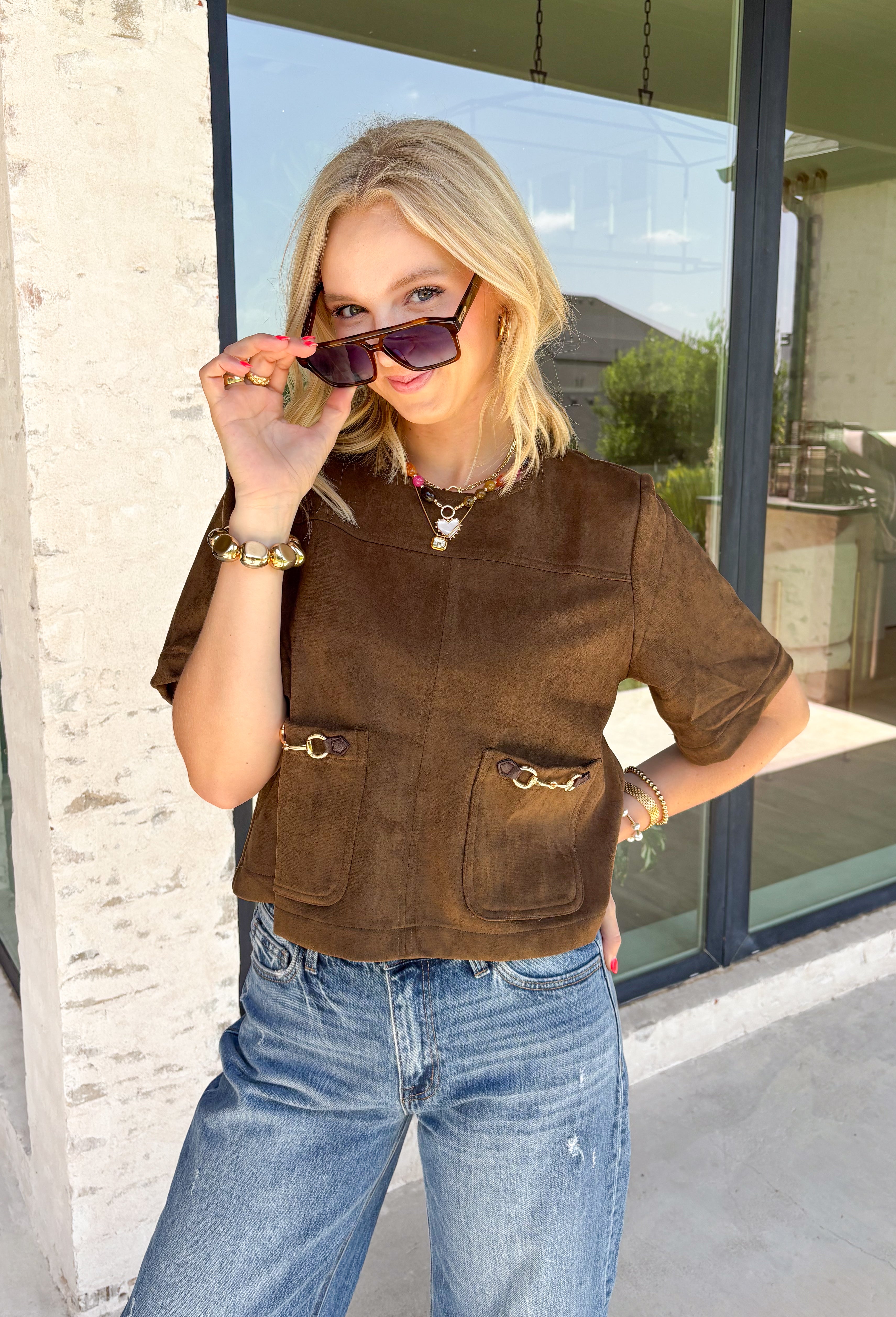 Elevate your autumn wardrobe with a top that's equal parts sophisticated and effortlessly wearable! Crafted from buttery-soft chocolate brown faux suede, this elevated piece brings rich texture and timeless style to any outfit. The standout gold horse bit details on the front pockets add an elegant equestrian-inspired touch, while the sleek back zipper closure creates a polished finish.
