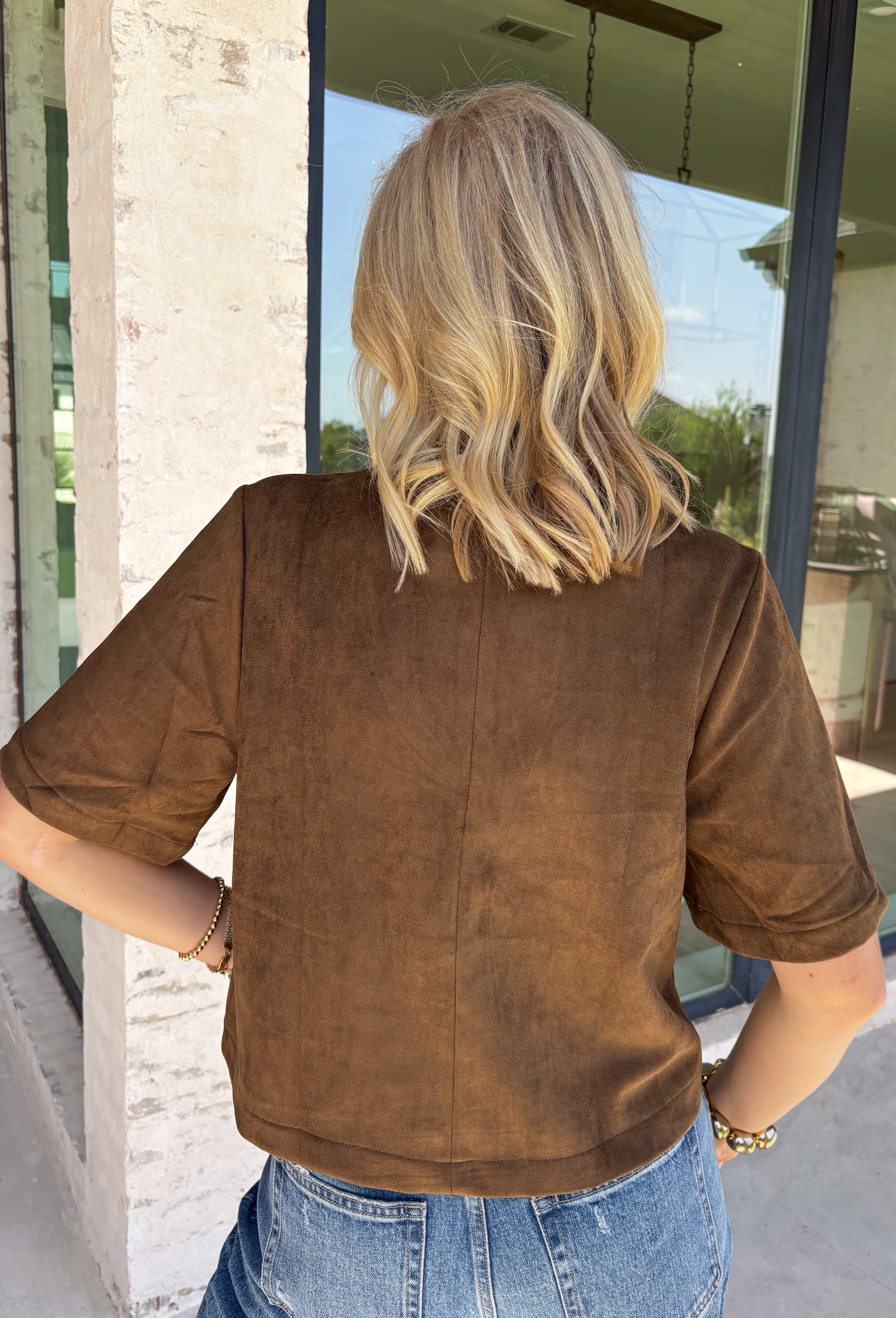 Elevate your autumn wardrobe with a top that's equal parts sophisticated and effortlessly wearable! Crafted from buttery-soft chocolate brown faux suede, this elevated piece brings rich texture and timeless style to any outfit. The standout gold horse bit details on the front pockets add an elegant equestrian-inspired touch, while the sleek back zipper closure creates a polished finish.