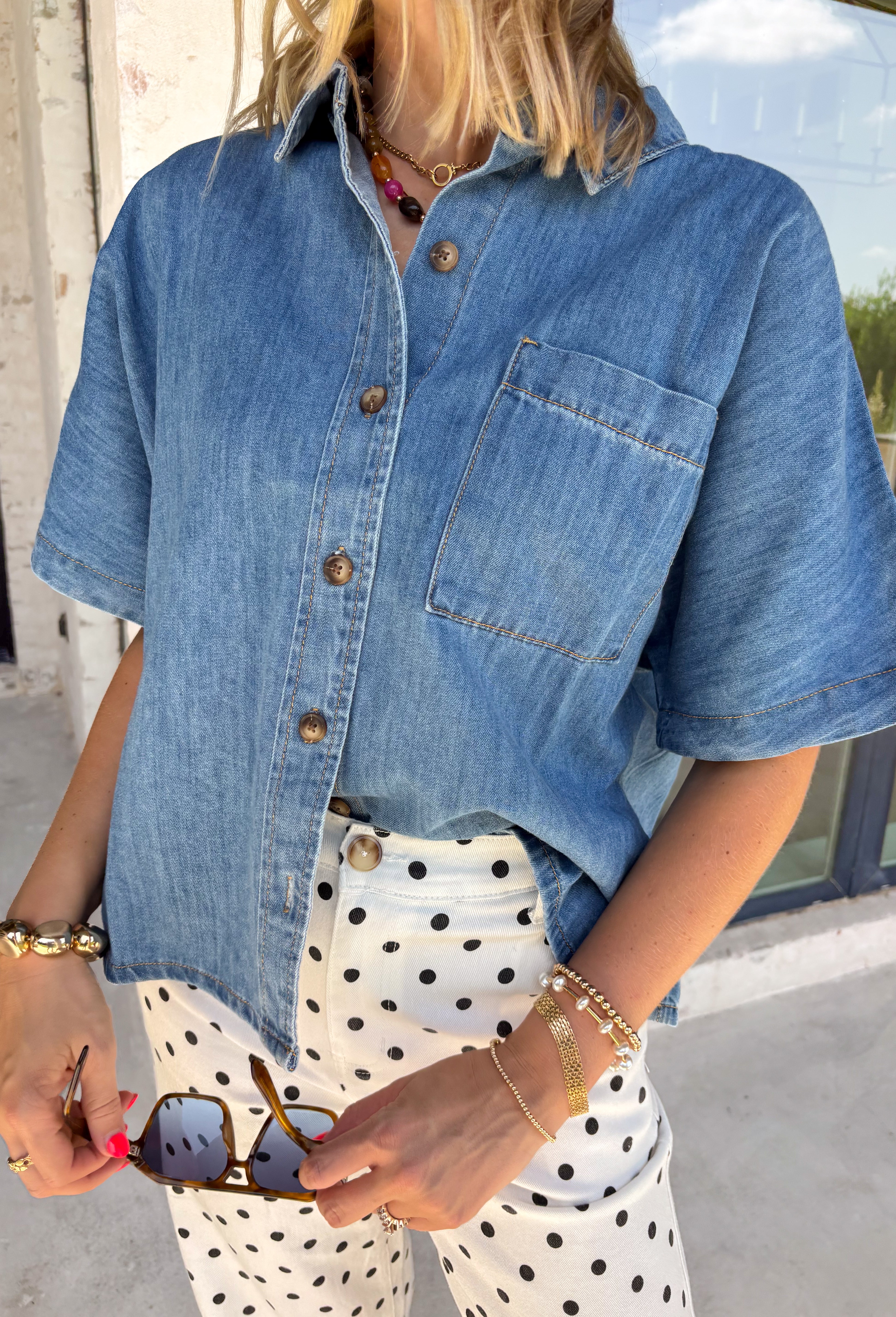 A timeless denim shirt is a wardrobe essential, and this one is designed to go with everything. Crafted from soft medium wash denim with warm tan contrast stitching throughout, this classic button-down top offers effortless style for every season. The collared neckline and front pocket give it a timeless look, while the short sleeves make it perfect for layering or wearing on its own. 