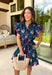 Bright, breezy, and made for spring plans, this navy dress by Entro is full of fun, feel-good color. Featuring a vibrant floral print with pops of purple, pink, green, and blue, it brings the perfect burst of spring energy to a classic navy base. The collared neckline and full button front give it a polished look, while flutter sleeves keep it light and feminine. Finished with contrast scallop trim along the edges, a waist tie for a flattering fit, and side pockets.