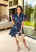 Bright, breezy, and made for spring plans, this navy dress by Entro is full of fun, feel-good color. Featuring a vibrant floral print with pops of purple, pink, green, and blue, it brings the perfect burst of spring energy to a classic navy base. The collared neckline and full button front give it a polished look, while flutter sleeves keep it light and feminine. Finished with contrast scallop trim along the edges, a waist tie for a flattering fit, and side pockets.
