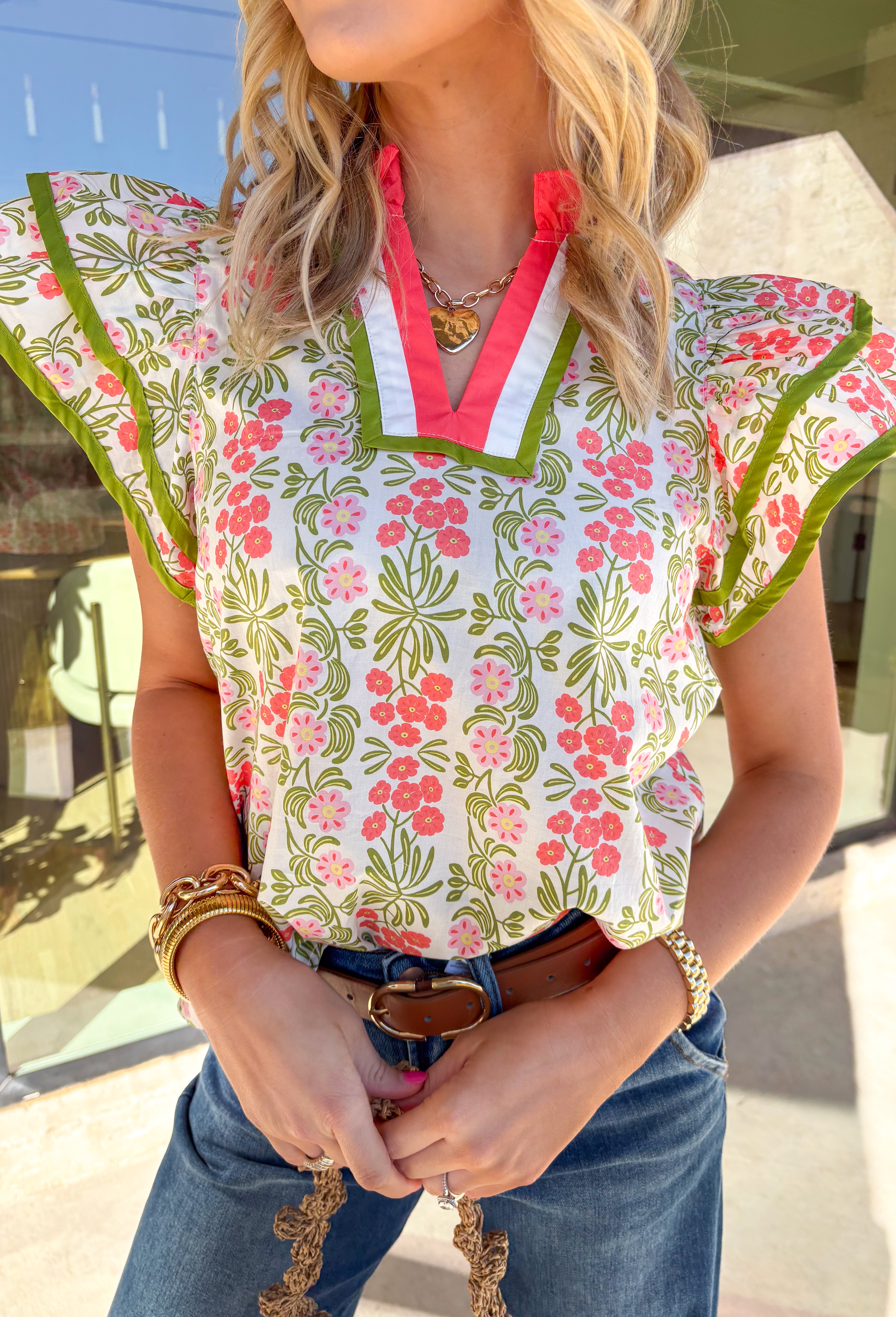 Soft, cheerful, and full of spring color, this cream short sleeve top by Entro is an easy way to brighten your everyday look. Featuring a pretty floral print with pops of green, pink, and coral, it feels light and happy for the season. The coral, white, and green band detail along the front adds a fun contrast, while the coral ruffle neckline gives it a sweet, feminine finish. Made from breathable cotton, this top is perfect for warm spring days.