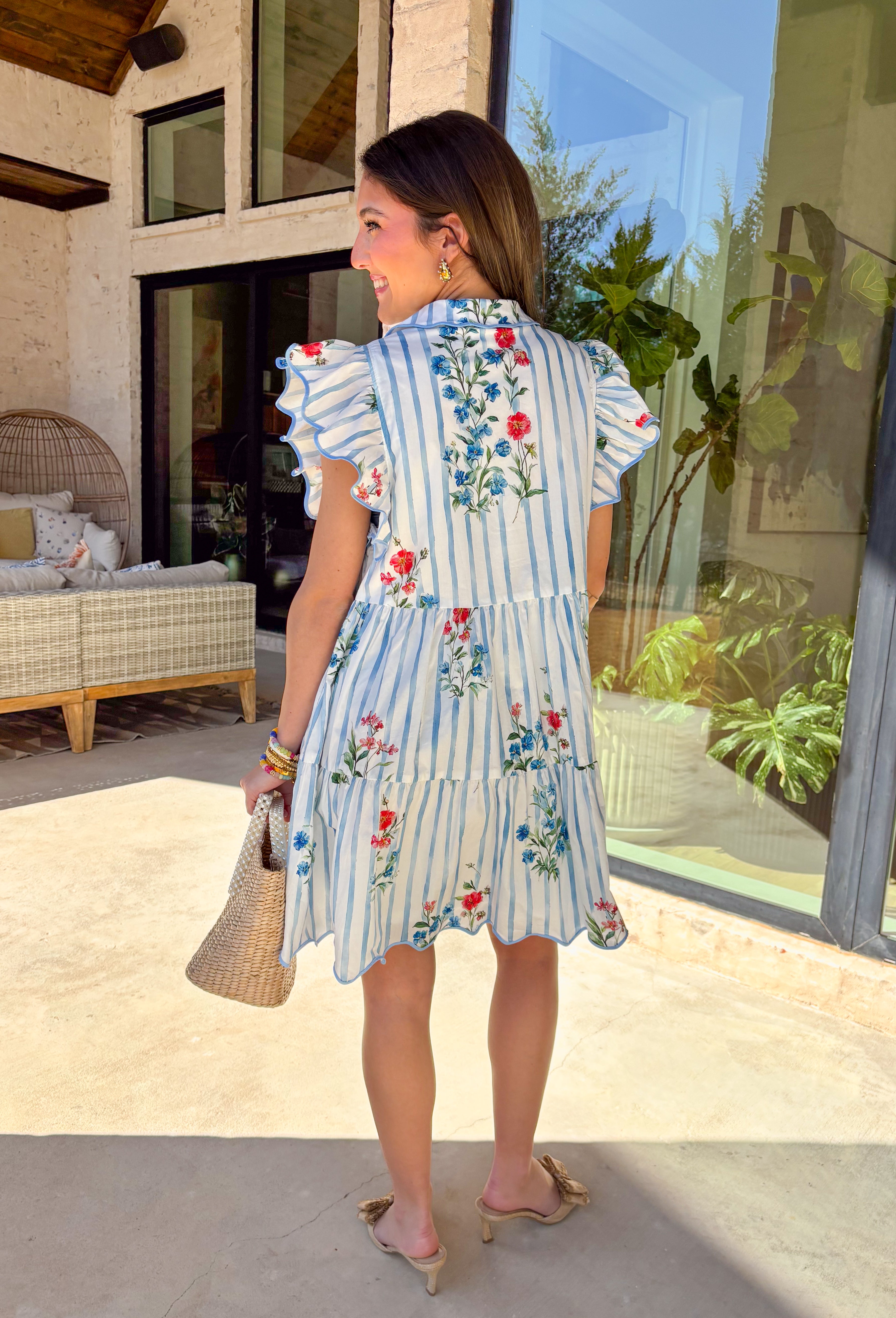 Fresh, playful, and full of spring charm, this button-down dress by Entro is a standout piece for the season. Featuring a classic blue and white stripe base with colorful floral prints layered throughout, it strikes the perfect balance between timeless and fun. Flutter sleeves add soft movement, while scalloped accent trim along the edges gives it a sweet, polished finish. Fully lined and made from breathable cotton, this dress is easy, comfortable, and perfect for sunny days ahead.