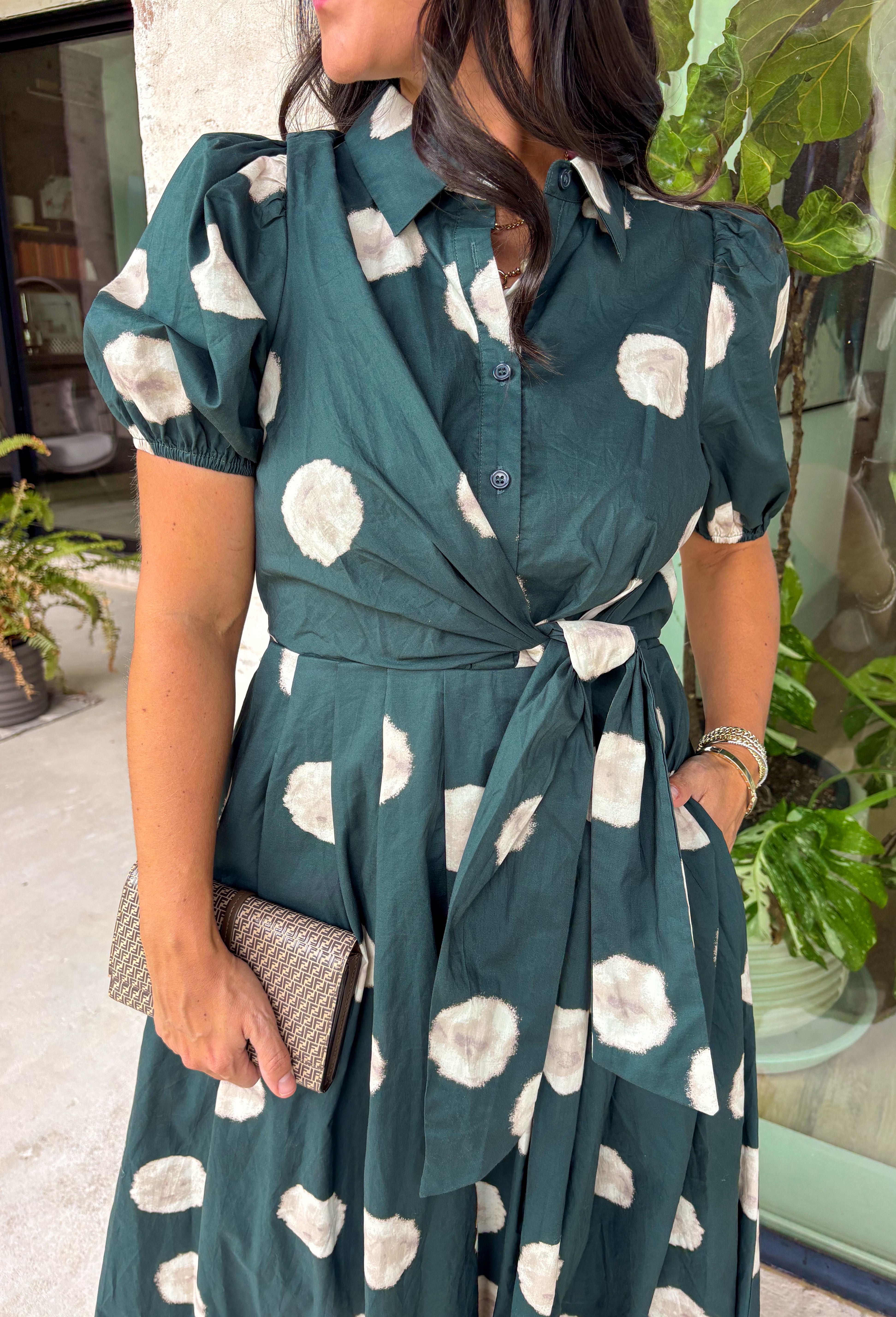 Timeless style meets effortless charm in this beautiful polka dot midi dress. Featuring a rich hunter green backdrop with a bold neutral polka dot print, this classic silhouette is one you'll love wearing year after year. The button-front design and adjustable self-tie waist create a flattering, feminine fit, while the puff sleeves add just the right amount of romantic detail. Complete with side pockets and a fully lined design, this cotton dress is as practical as it is polished.