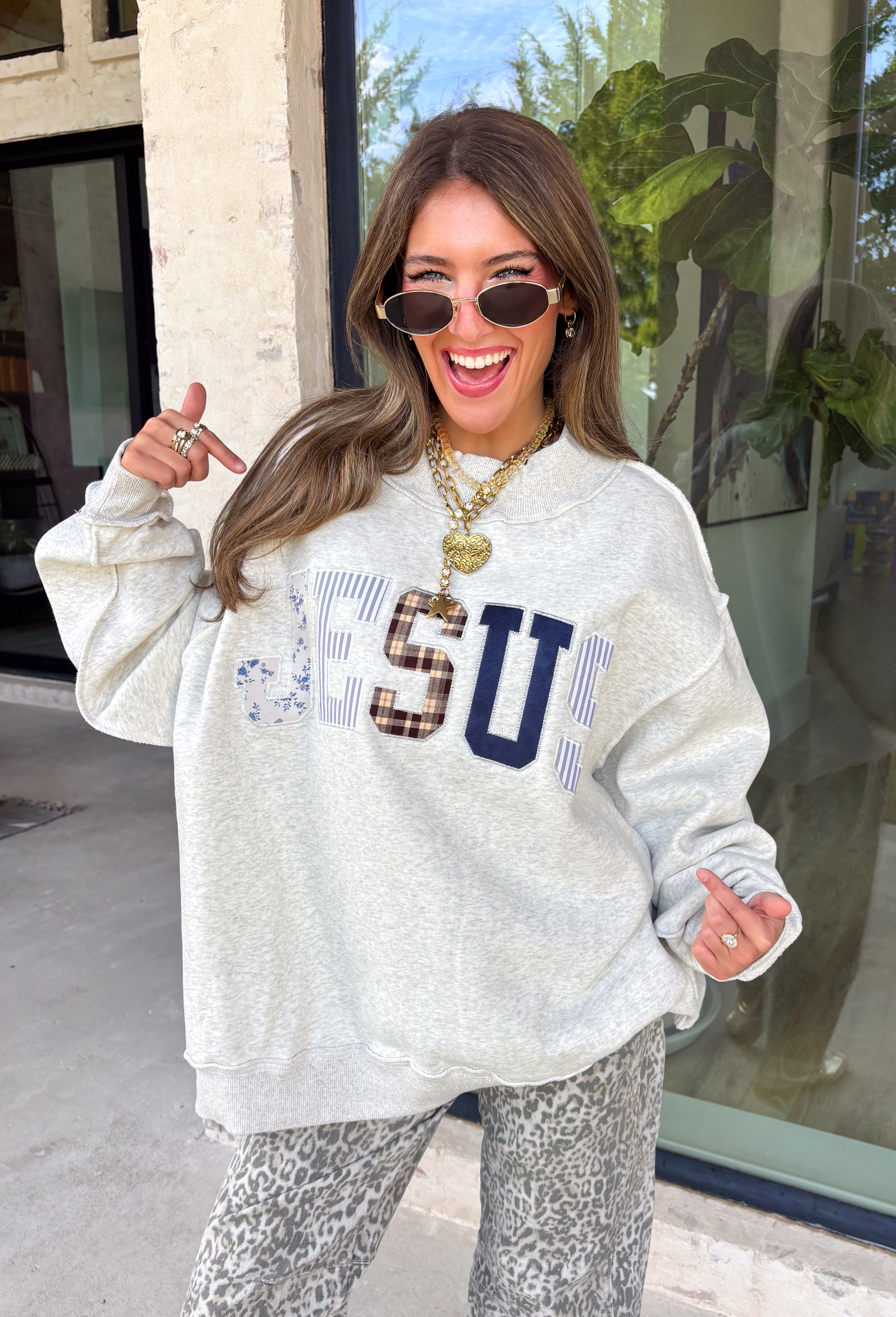 Wear your faith in the coziest way with this heather grey “Jesus” pullover from Bucket List. Each letter features its own unique print, including dainty florals, classic stripes, plaid, and solid navy in a soft mix of neutrals and shades of blue. Light grey embroidery outlines each letter for an extra touch of texture that makes the design stand out beautifully against the heather grey background. 