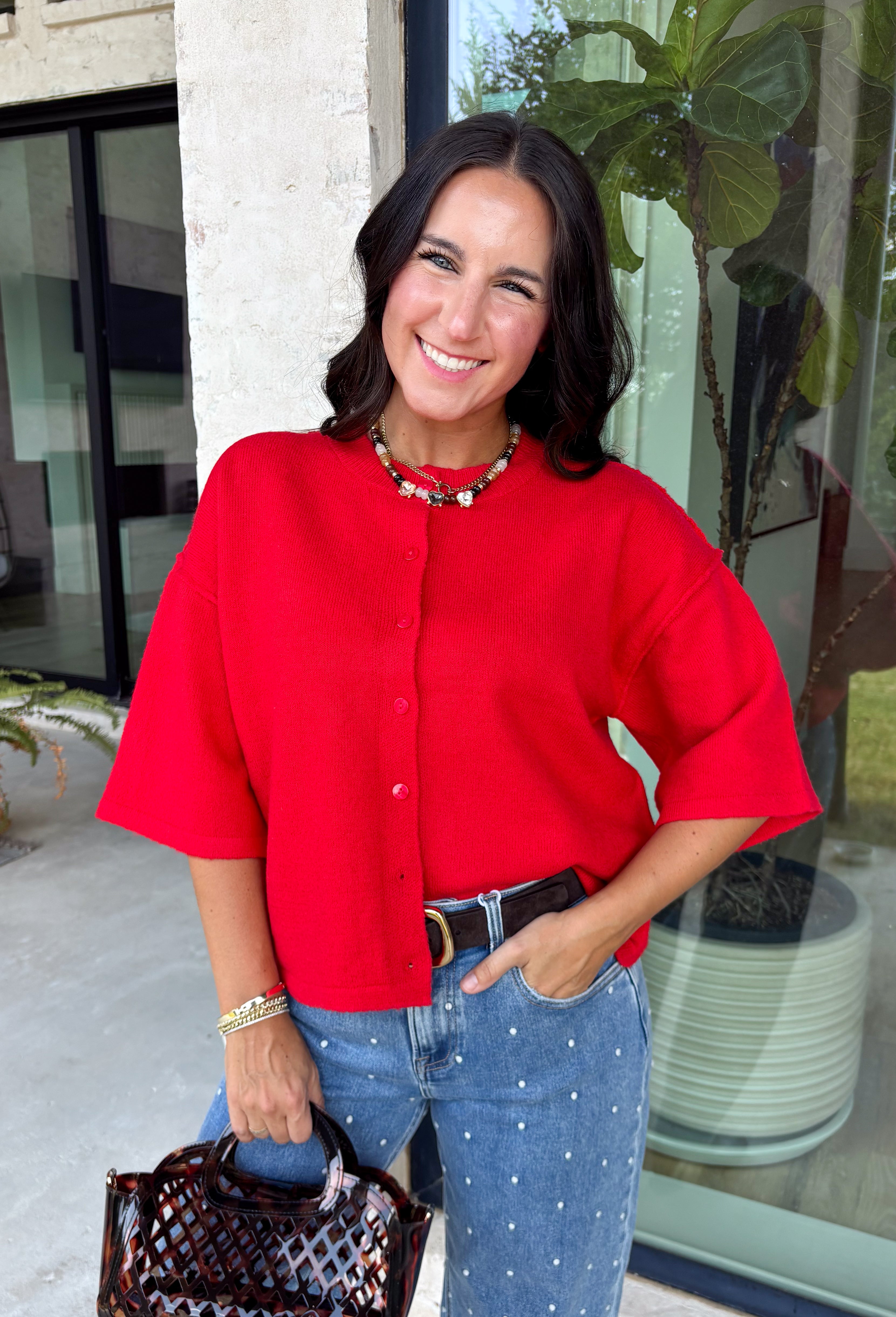 Add a timeless staple to your wardrobe with this cozy cardigan from Double Zero. Designed in a rich red hue, this short sleeve knit is the perfect combination of classic style and everyday comfort. The button-front design makes it easy to wear on its own as a sweater or layered over your favorite basics, while the ribbed neckline adds a polished finishing touch. Soft, versatile, and easy to style, this cardigan is one you'll find yourself reaching for all season long.