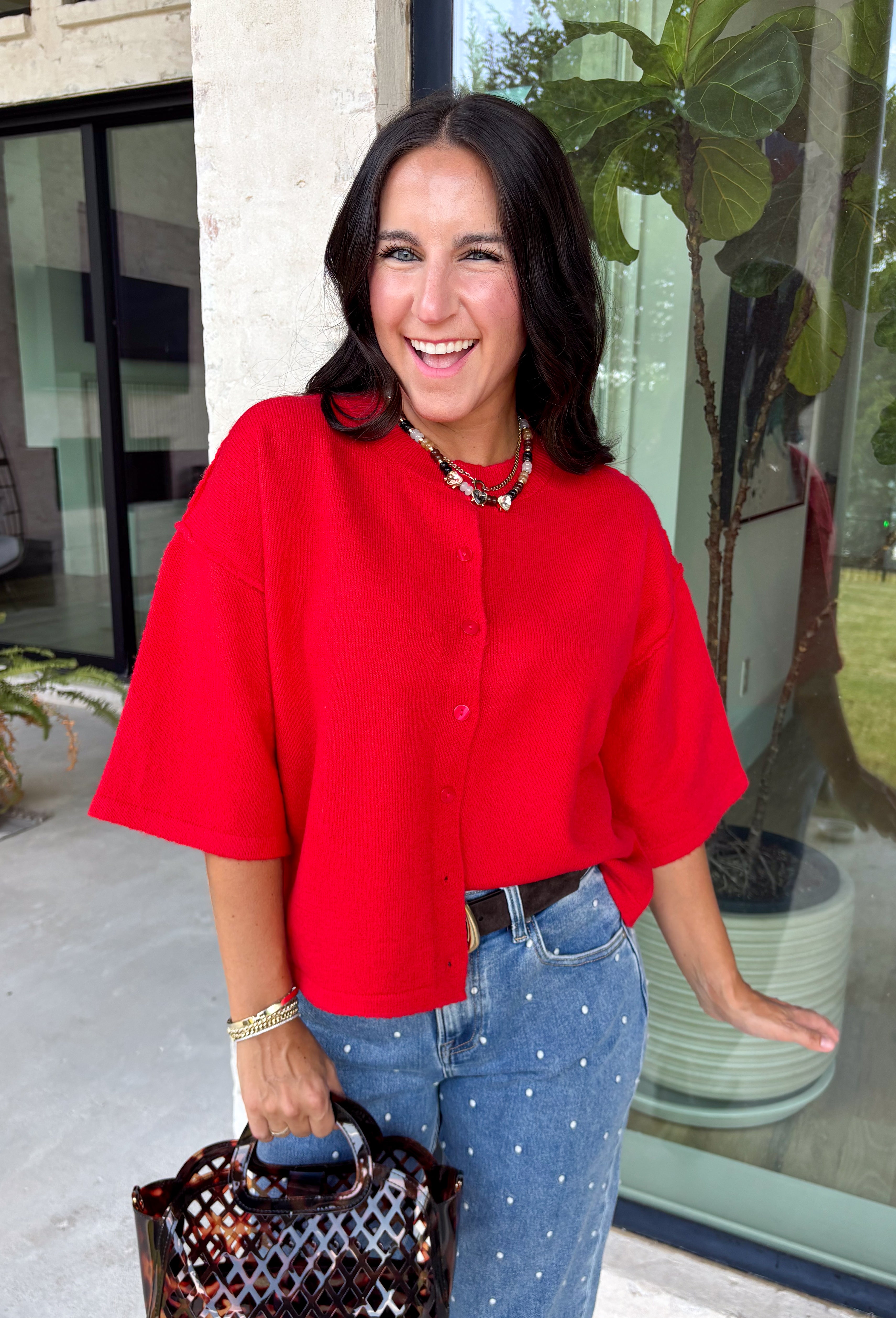 Add a timeless staple to your wardrobe with this cozy cardigan from Double Zero. Designed in a rich red hue, this short sleeve knit is the perfect combination of classic style and everyday comfort. The button-front design makes it easy to wear on its own as a sweater or layered over your favorite basics, while the ribbed neckline adds a polished finishing touch. Soft, versatile, and easy to style, this cardigan is one you'll find yourself reaching for all season long.