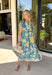 Bold, bright, and full of personality — this blue midi dress is made to stand out. The colorful floral print features shades of yellow, green, blue, and white, giving it that fresh, sunshine-ready feel. What makes it extra special? The contrasting abstract print in orange, pink, and blue along the front, sleeves, and hem for a playful pop of color that truly sets it apart. 
