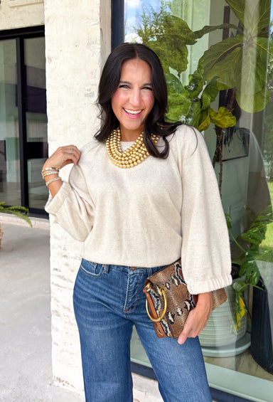 Nothing says cozy season quite like the perfect neutral sweater. Crafted in a soft oatmeal hue, this elevated knit is designed with beautifully oversized sleeves that create a relaxed, effortlessly chic silhouette. The ribbed neckline and hem add timeless structure, while the elastic cuffs give the sleeves a soft, billowy shape.