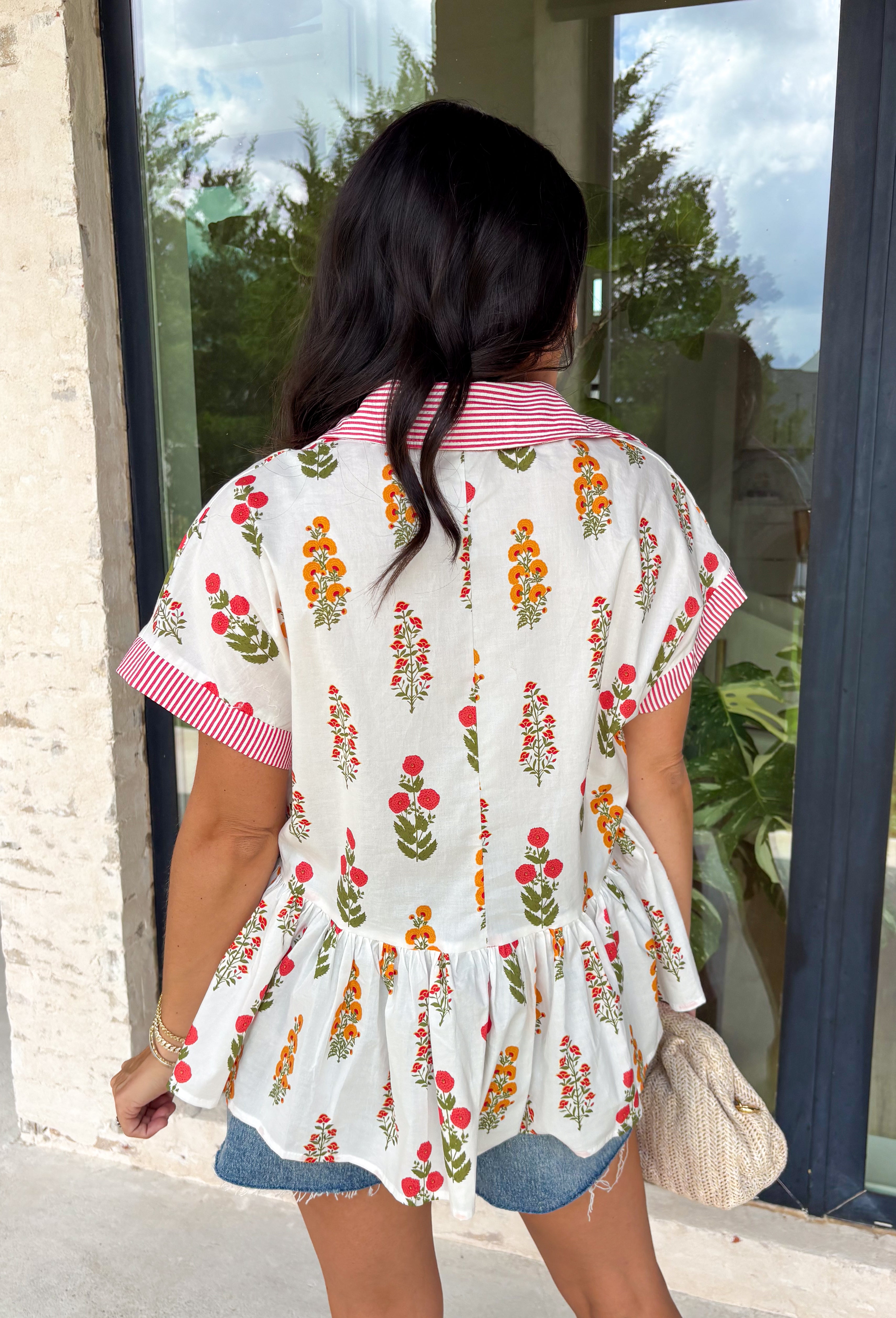 This white babydoll top is the perfect mix of playful and feminine for summer! The colorful floral print in yellow, red, and green brings a bright, happy feel, while the red and white stripe detail on the collar and sleeves adds the cutest pop of contrast. The babydoll silhouette keeps it light, breezy, and easy to wear, and the front button details give it that extra touch of charm. Made from breathable cotton, it’s perfect for warm days when you want something effortless but still fun.