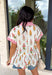 This white babydoll top is the perfect mix of playful and feminine for summer! The colorful floral print in yellow, red, and green brings a bright, happy feel, while the red and white stripe detail on the collar and sleeves adds the cutest pop of contrast. The babydoll silhouette keeps it light, breezy, and easy to wear, and the front button details give it that extra touch of charm. Made from breathable cotton, it’s perfect for warm days when you want something effortless but still fun.