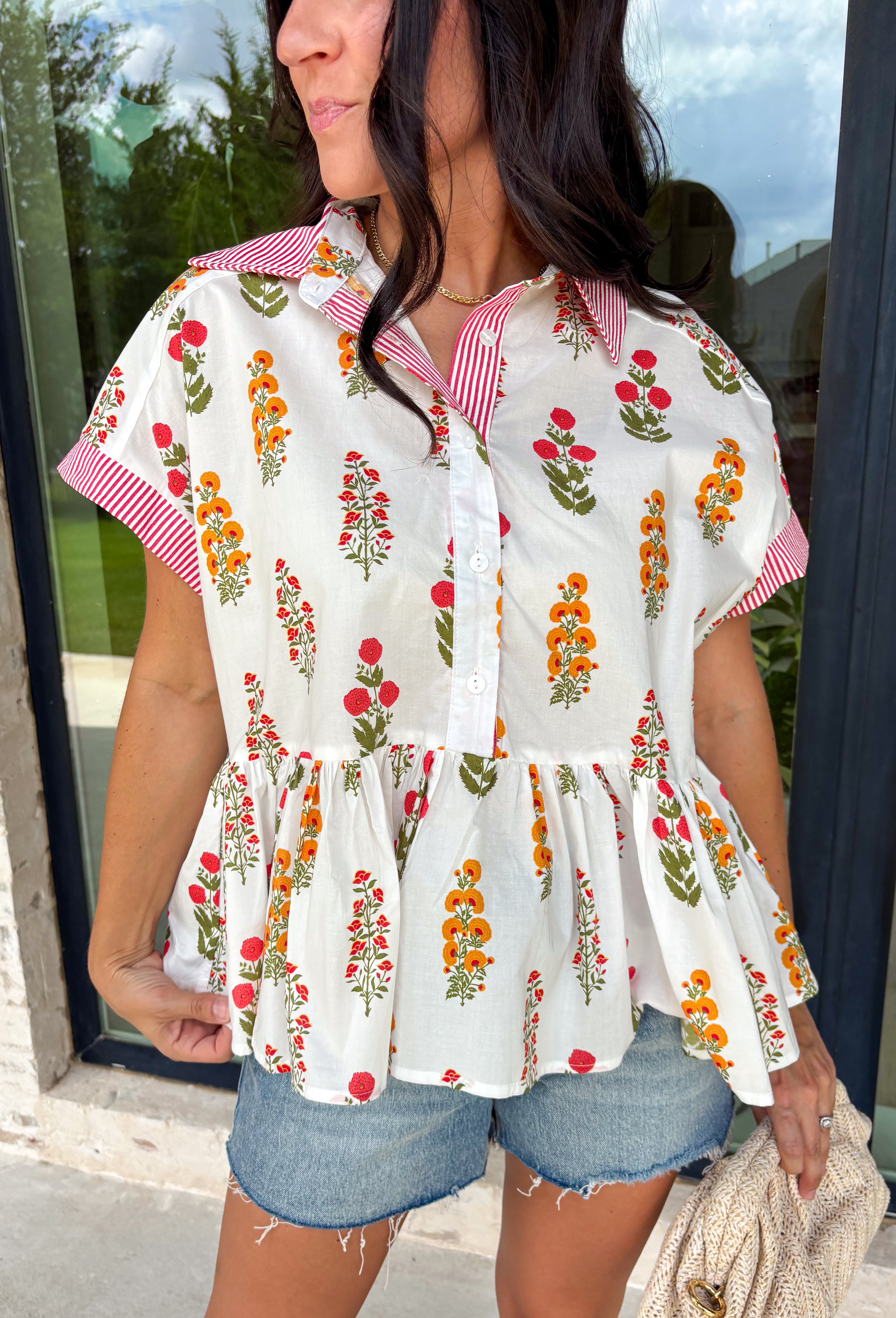 This white babydoll top is the perfect mix of playful and feminine for summer! The colorful floral print in yellow, red, and green brings a bright, happy feel, while the red and white stripe detail on the collar and sleeves adds the cutest pop of contrast. The babydoll silhouette keeps it light, breezy, and easy to wear, and the front button details give it that extra touch of charm. Made from breathable cotton, it’s perfect for warm days when you want something effortless but still fun.