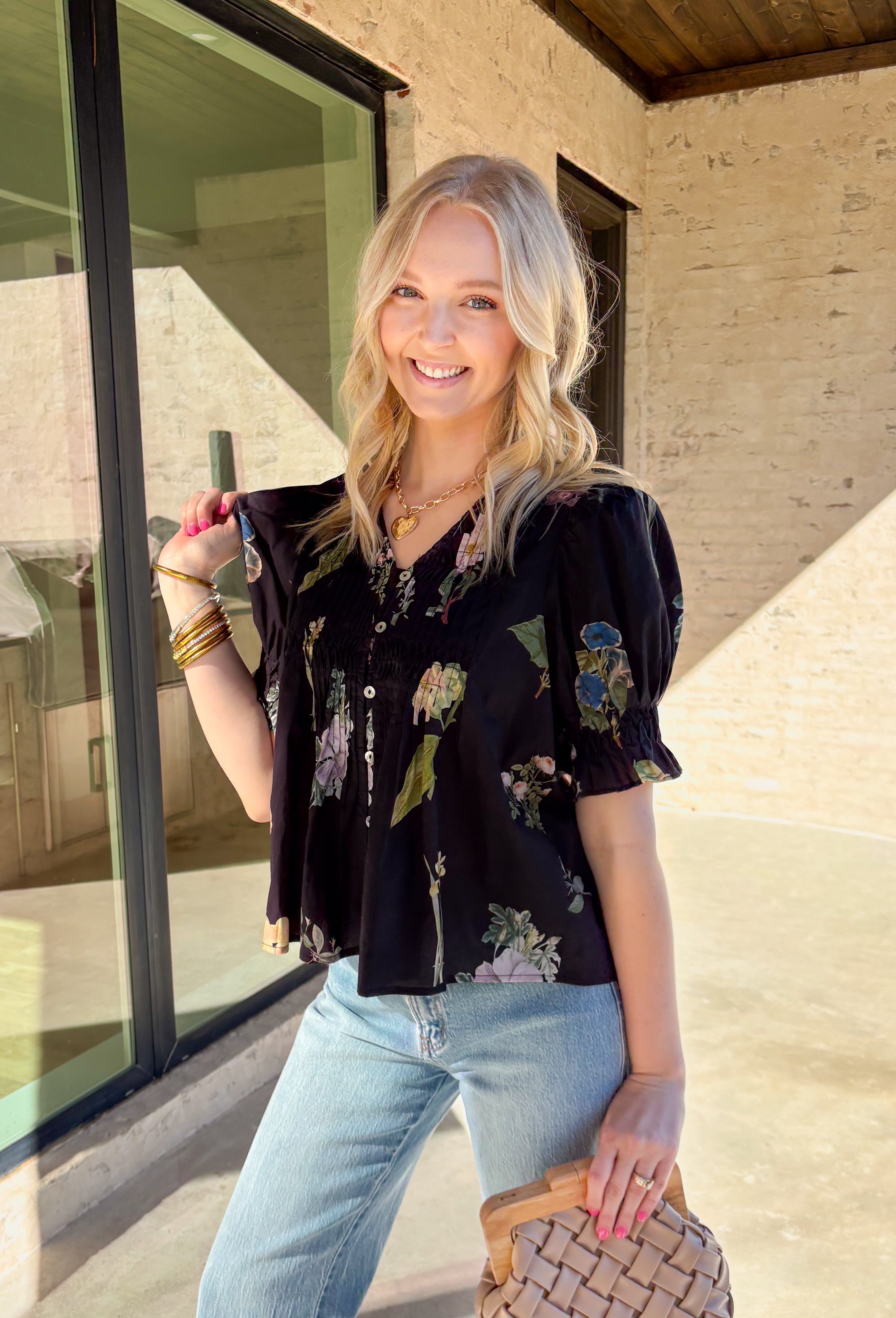 Classic with a spring refresh, this black short sleeve top by Entro is an easy standout. Featuring a soft floral print with pops of blush, green, and blue, it adds just the right amount of color to a timeless silhouette. The button-down front and pleating detail along the front give it a polished, flattering look, while the lightweight cotton fabric keeps it breathable and comfortable for warmer days.