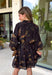 Step into the season with effortless style in this beautifully detailed dress from Entro. Designed with a classic black backdrop and a rich floral print in shades of brown and tan, this timeless dress captures the warmth of fall with every detail. The flattering v-neckline and button-front design create a polished silhouette, while the included matching belt defines the waist for a customizable fit. Finished with ¾ balloon sleeves, a playful ruffle hem, convenient side pockets.