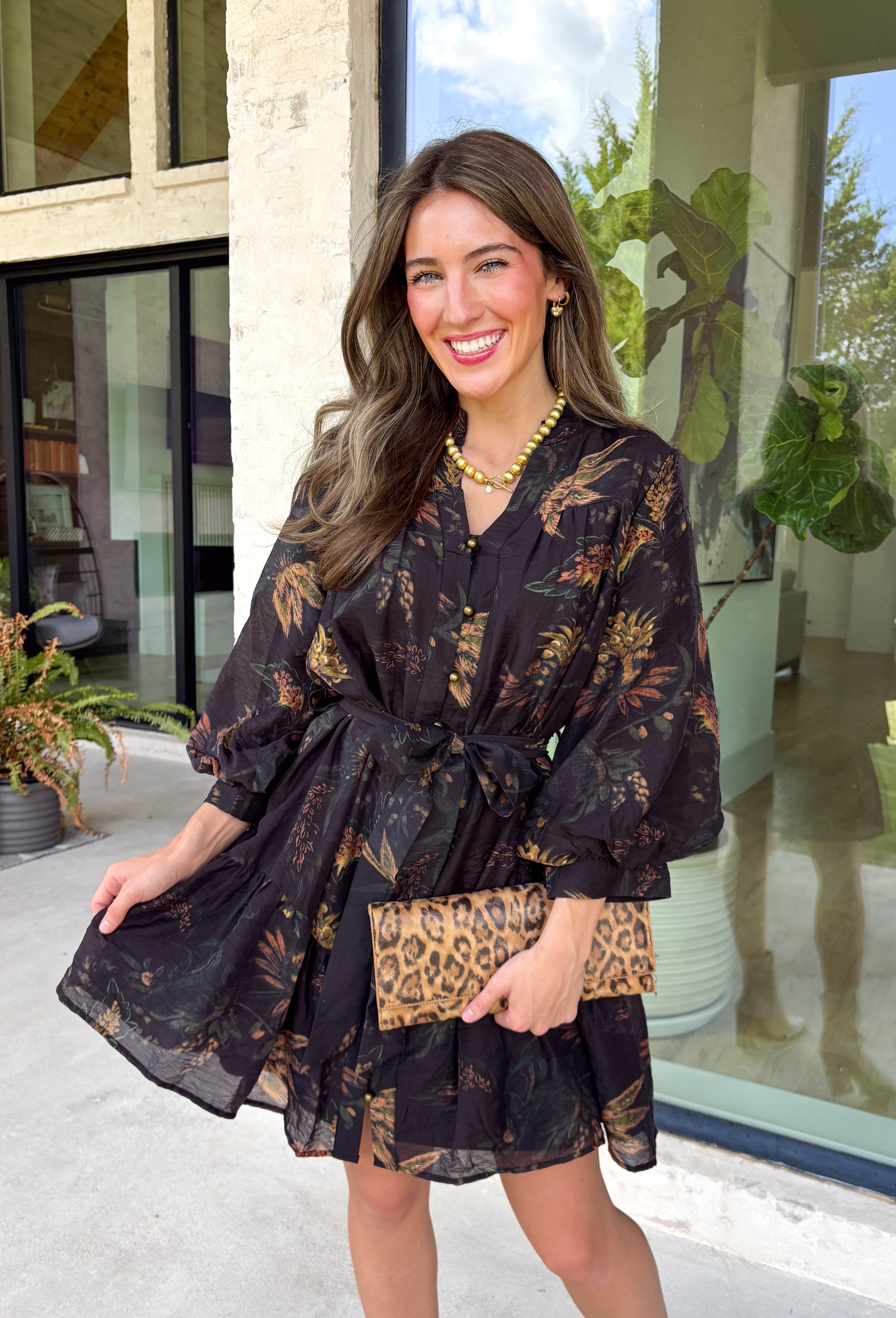 Step into the season with effortless style in this beautifully detailed dress from Entro. Designed with a classic black backdrop and a rich floral print in shades of brown and tan, this timeless dress captures the warmth of fall with every detail. The flattering v-neckline and button-front design create a polished silhouette, while the included matching belt defines the waist for a customizable fit. Finished with ¾ balloon sleeves, a playful ruffle hem, convenient side pockets.