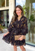 Step into the season with effortless style in this beautifully detailed dress from Entro. Designed with a classic black backdrop and a rich floral print in shades of brown and tan, this timeless dress captures the warmth of fall with every detail. The flattering v-neckline and button-front design create a polished silhouette, while the included matching belt defines the waist for a customizable fit. Finished with ¾ balloon sleeves, a playful ruffle hem, convenient side pockets.