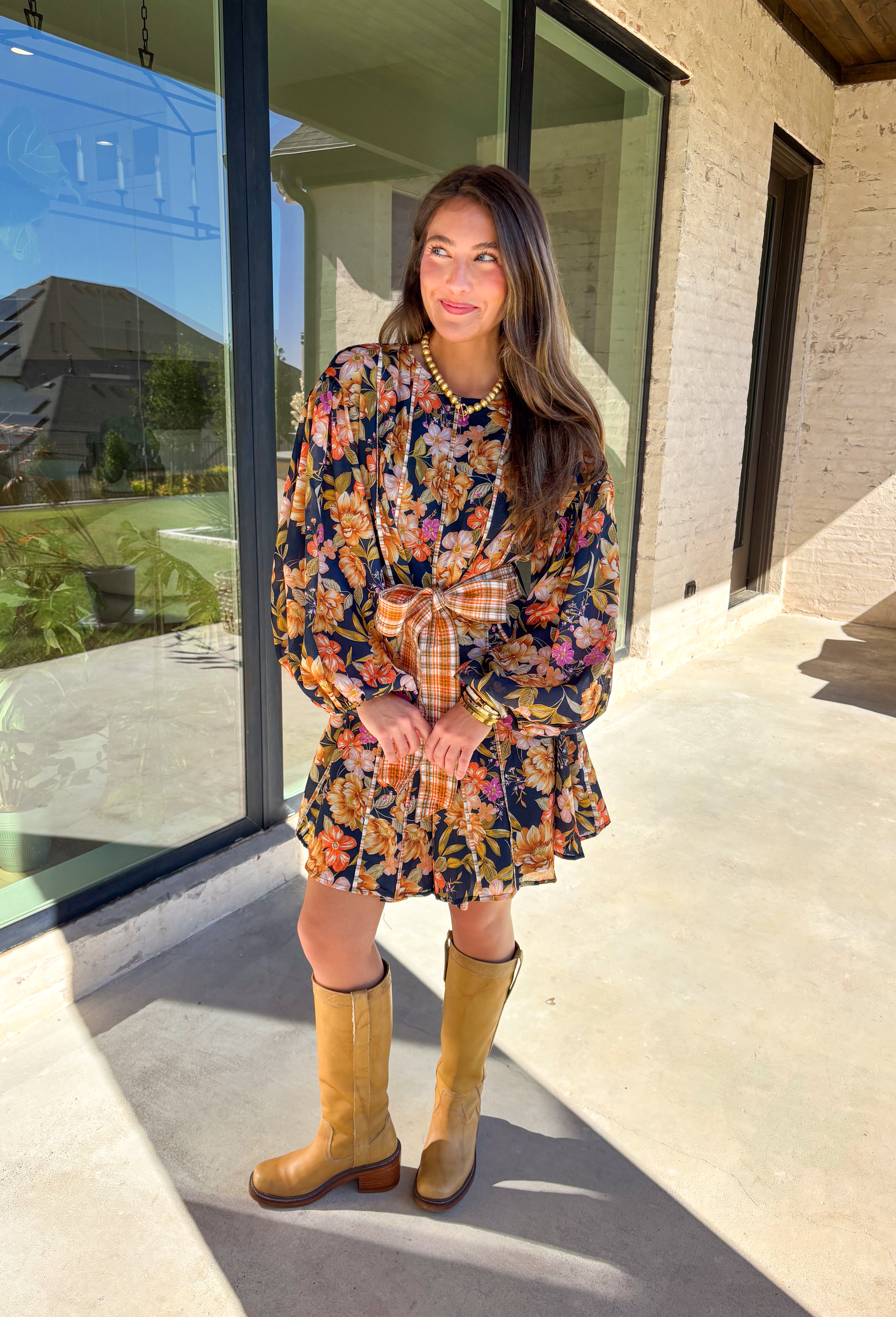 Bring bold fall energy to your wardrobe with this navy long sleeve dress featuring a colorful floral print in rich autumn shades. A playful orange plaid self-tie belt cinches the waist for a flattering finish, while striped piping throughout ties the look together with unique detail. The elastic cuff sleeves keep the fit comfortable, and the lightweight fabric makes it easy to wear through the season. Effortlessly fun and polished, this dress is a perfect choice for fall outings and gatherings.