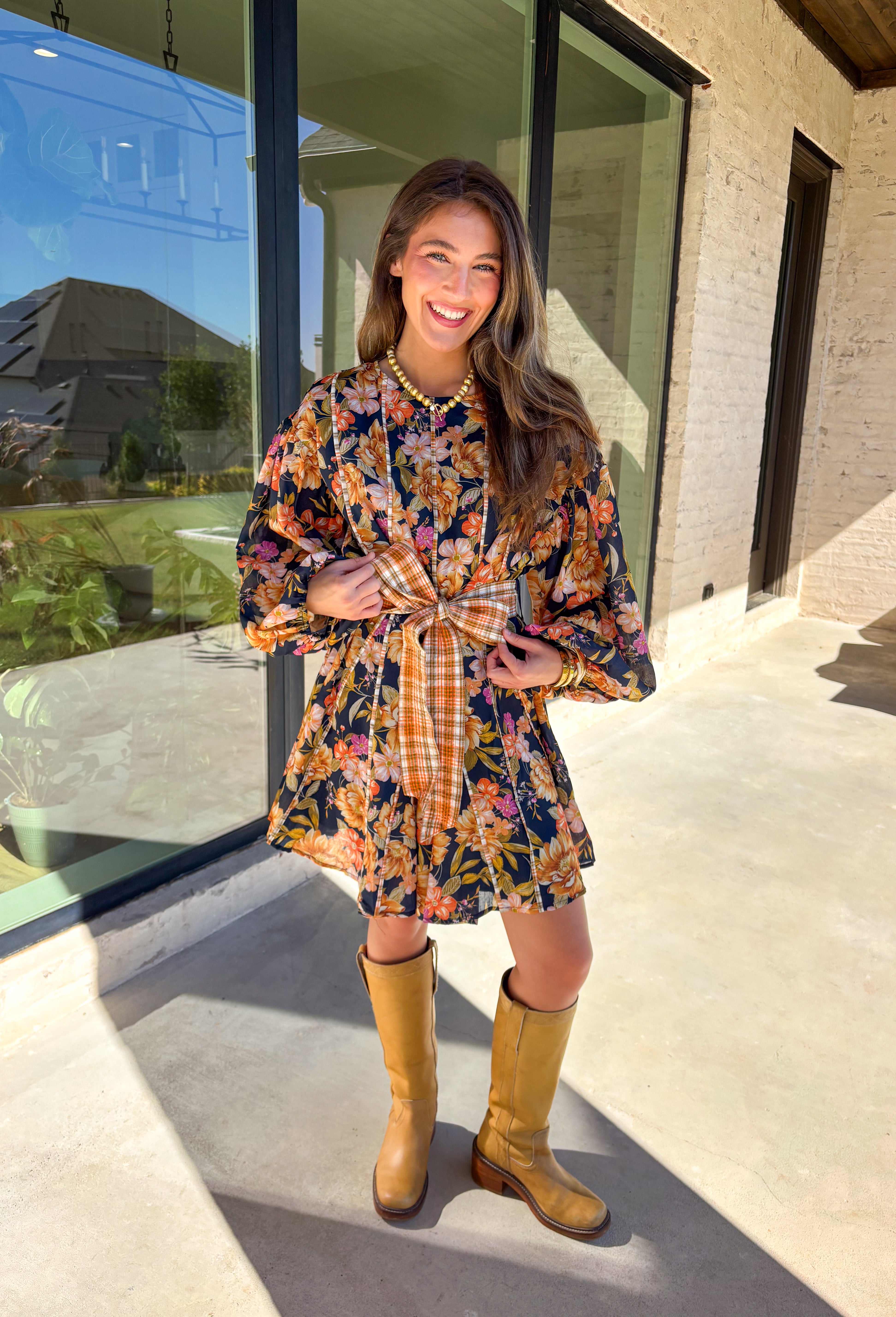 Bring bold fall energy to your wardrobe with this navy long sleeve dress featuring a colorful floral print in rich autumn shades. A playful orange plaid self-tie belt cinches the waist for a flattering finish, while striped piping throughout ties the look together with unique detail. The elastic cuff sleeves keep the fit comfortable, and the lightweight fabric makes it easy to wear through the season. Effortlessly fun and polished, this dress is a perfect choice for fall outings and gatherings.