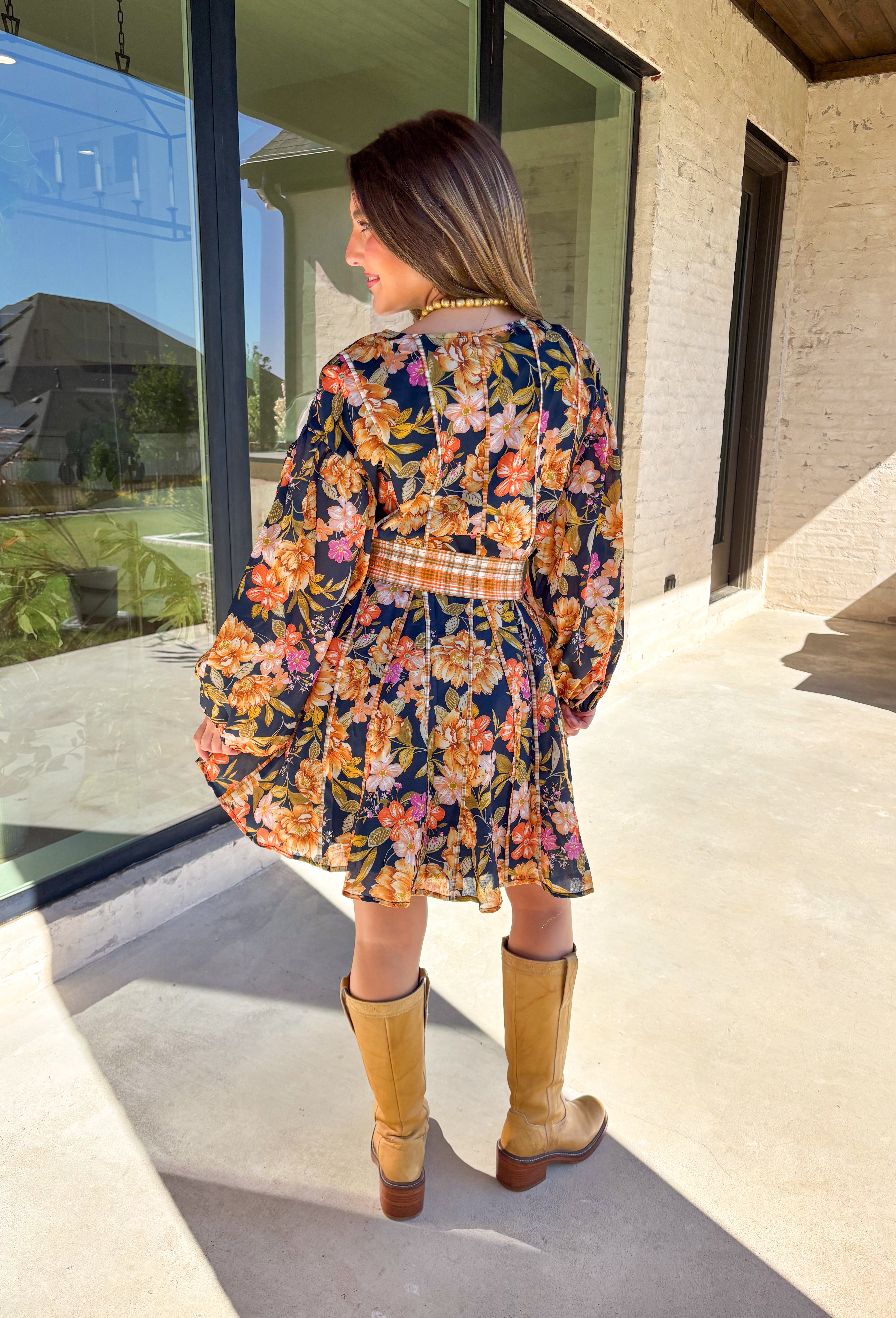 Bring bold fall energy to your wardrobe with this navy long sleeve dress featuring a colorful floral print in rich autumn shades. A playful orange plaid self-tie belt cinches the waist for a flattering finish, while striped piping throughout ties the look together with unique detail. The elastic cuff sleeves keep the fit comfortable, and the lightweight fabric makes it easy to wear through the season. Effortlessly fun and polished, this dress is a perfect choice for fall outings and gatherings.