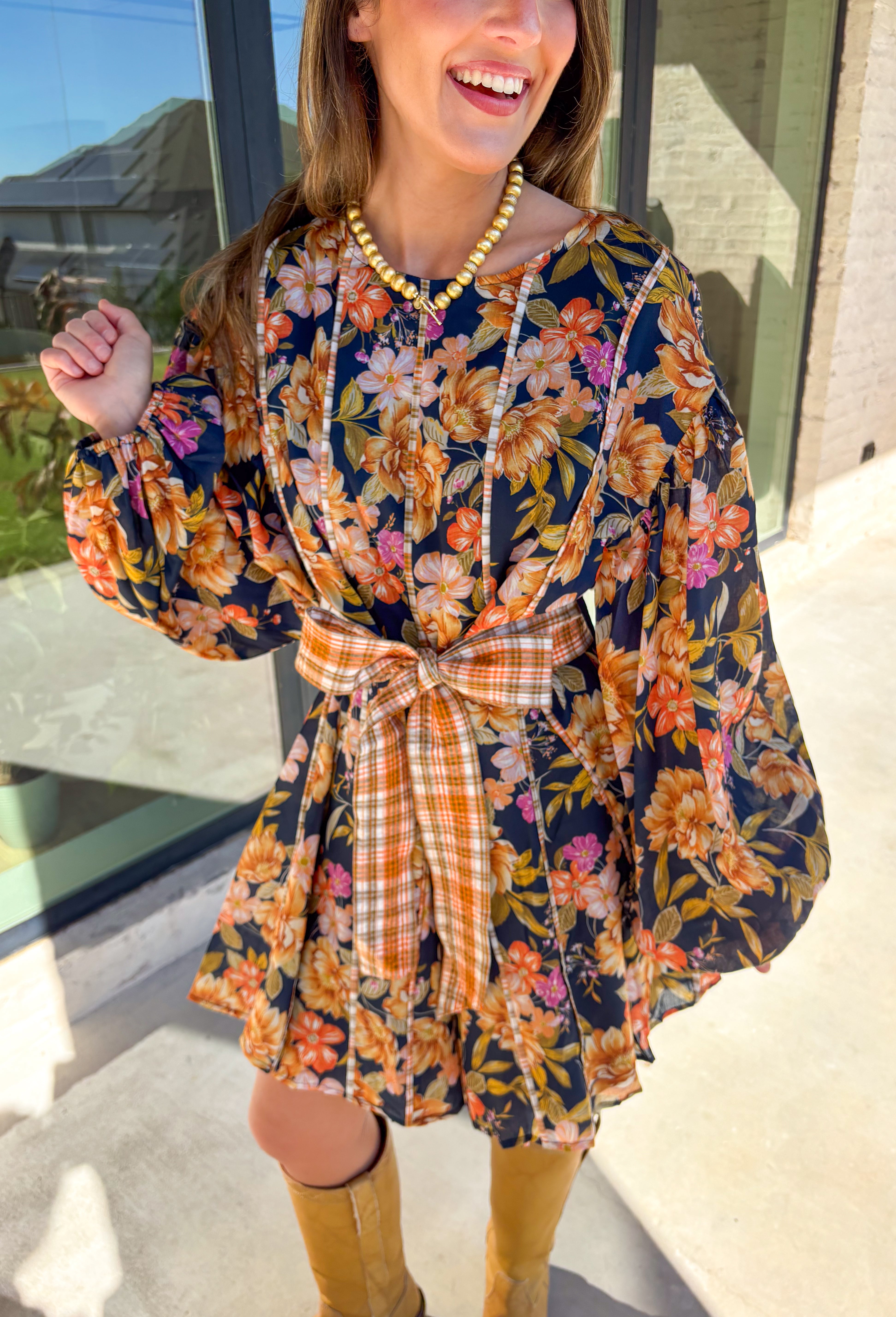Bring bold fall energy to your wardrobe with this navy long sleeve dress featuring a colorful floral print in rich autumn shades. A playful orange plaid self-tie belt cinches the waist for a flattering finish, while striped piping throughout ties the look together with unique detail. The elastic cuff sleeves keep the fit comfortable, and the lightweight fabric makes it easy to wear through the season. Effortlessly fun and polished, this dress is a perfect choice for fall outings and gatherings.