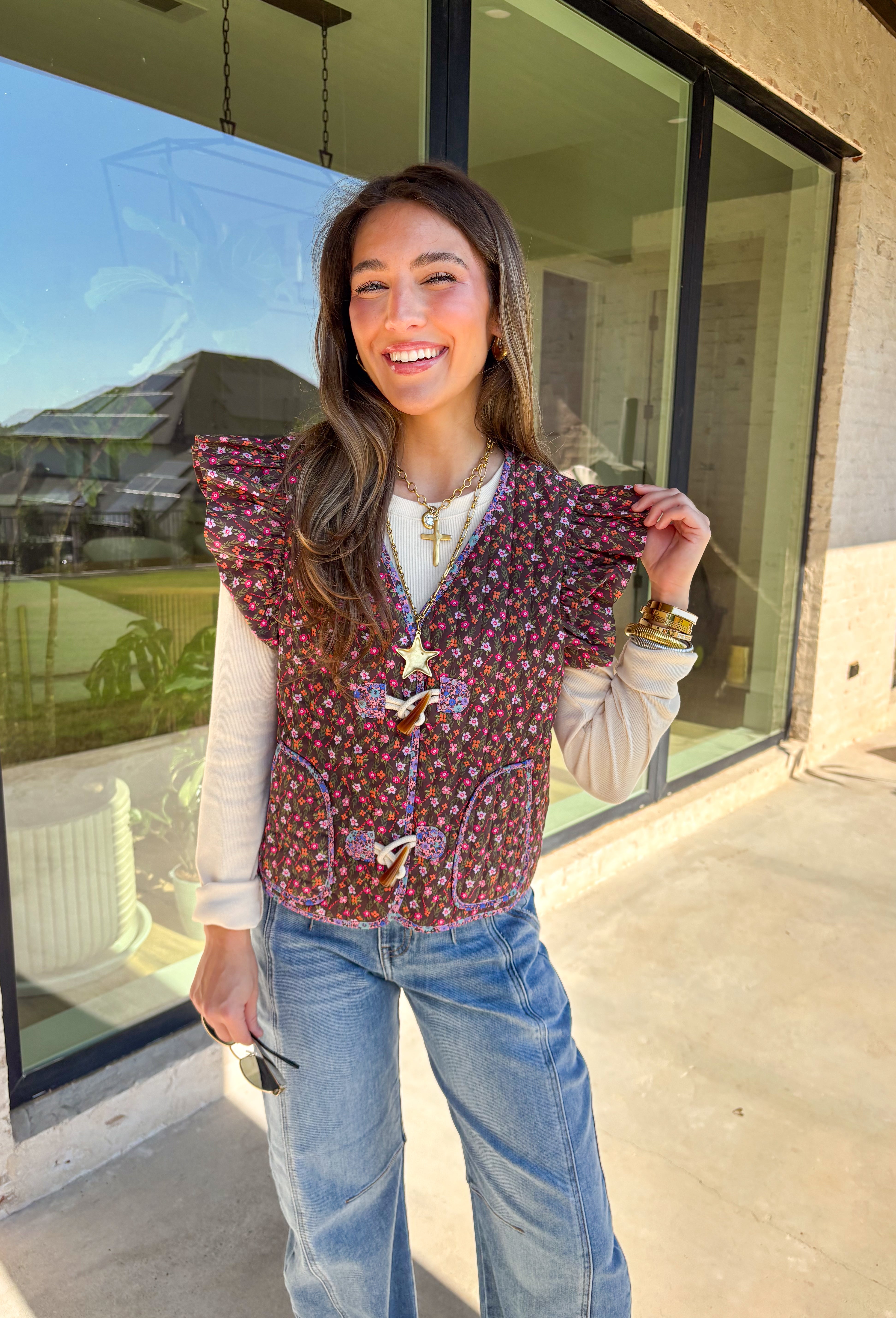 This charming quilted vest is giving all the cozy fall vibes with a pop of cheerful color. The brown base is covered in a dainty floral print in soft shades of pink, orange, and green—perfect for layering over your favorite long sleeve tops. Ruffle sleeves and oversized button closures add just the right amount of whimsy!
