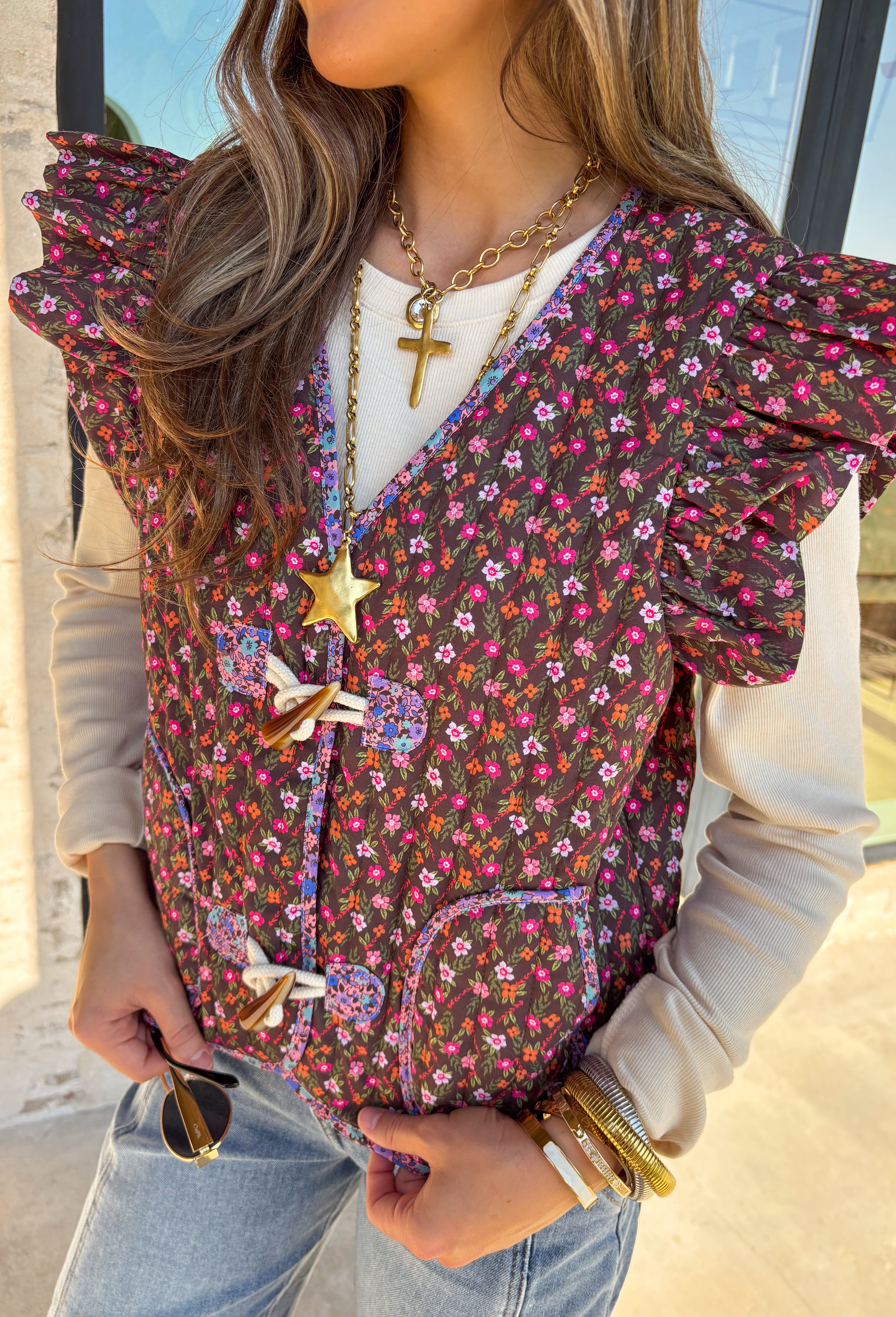 This charming quilted vest is giving all the cozy fall vibes with a pop of cheerful color. The brown base is covered in a dainty floral print in soft shades of pink, orange, and green—perfect for layering over your favorite long sleeve tops. Ruffle sleeves and oversized button closures add just the right amount of whimsy!