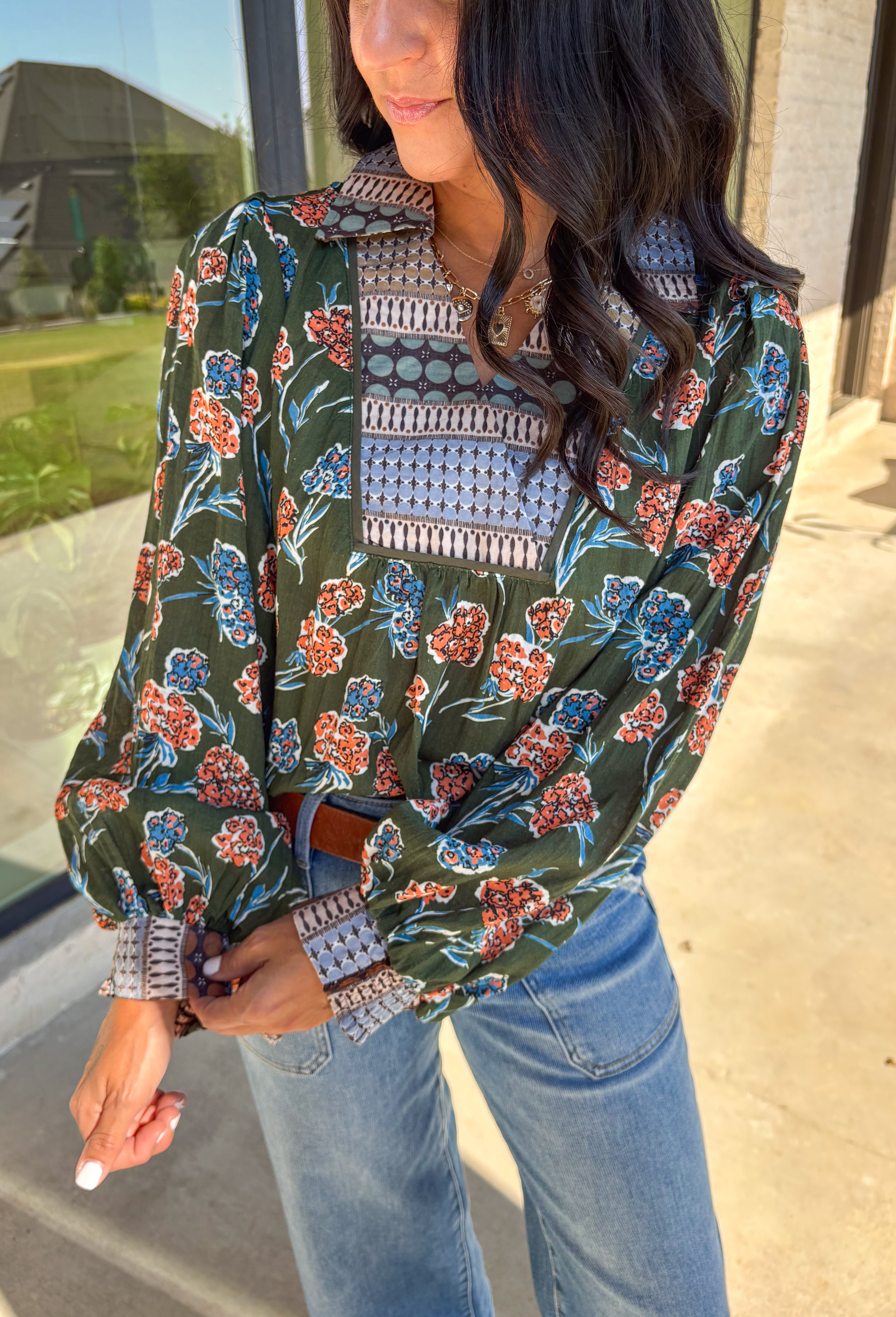 This green long sleeve top is a fresh mix of bold florals and thoughtful detail. Splashed with a colorful floral print in shades of orange, blue, black, and white, it’s balanced with a neutral abstract print along the front and collar for extra visual interest. Smocked sleeves finish the look with a feminine touch, making this blouse a statement piece you’ll love wearing through the season. Lightweight and easy to style, it’s perfect for everything from weekday wear to weekend outings.