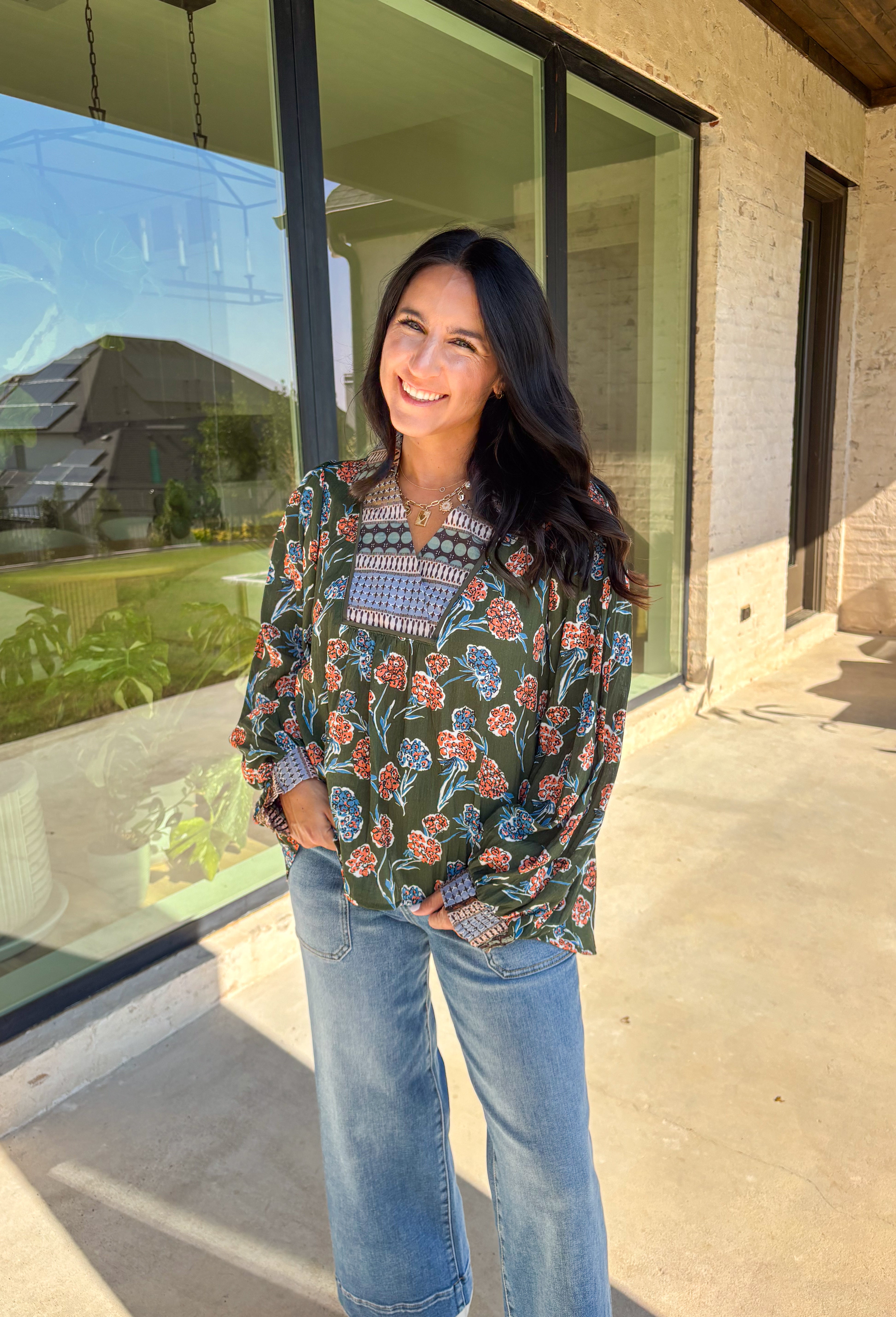 This green long sleeve top is a fresh mix of bold florals and thoughtful detail. Splashed with a colorful floral print in shades of orange, blue, black, and white, it’s balanced with a neutral abstract print along the front and collar for extra visual interest. Smocked sleeves finish the look with a feminine touch, making this blouse a statement piece you’ll love wearing through the season. Lightweight and easy to style, it’s perfect for everything from weekday wear to weekend outings.